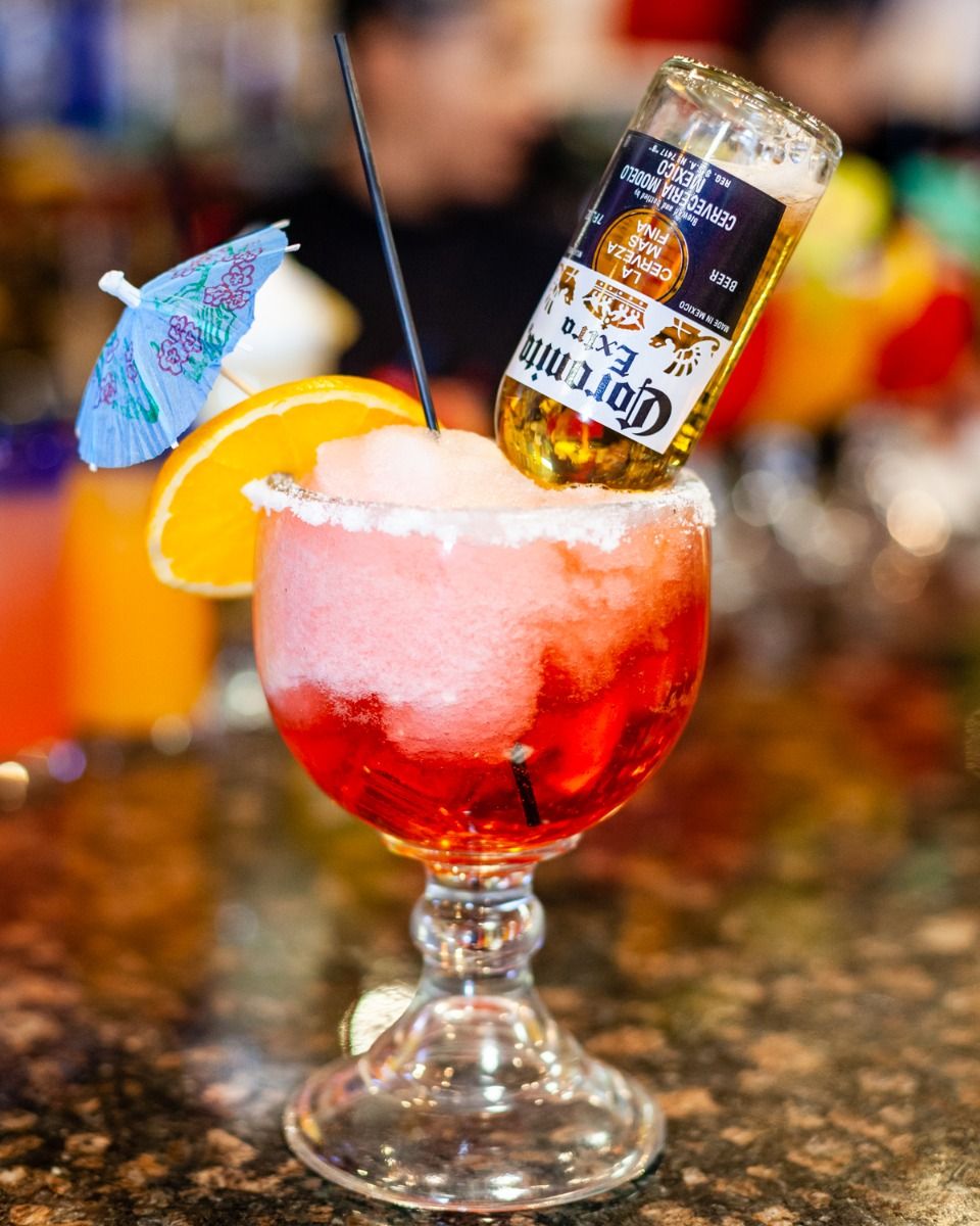 Margarita-style cocktail with a Corona beer bottle, orange slice, and umbrella garnish.