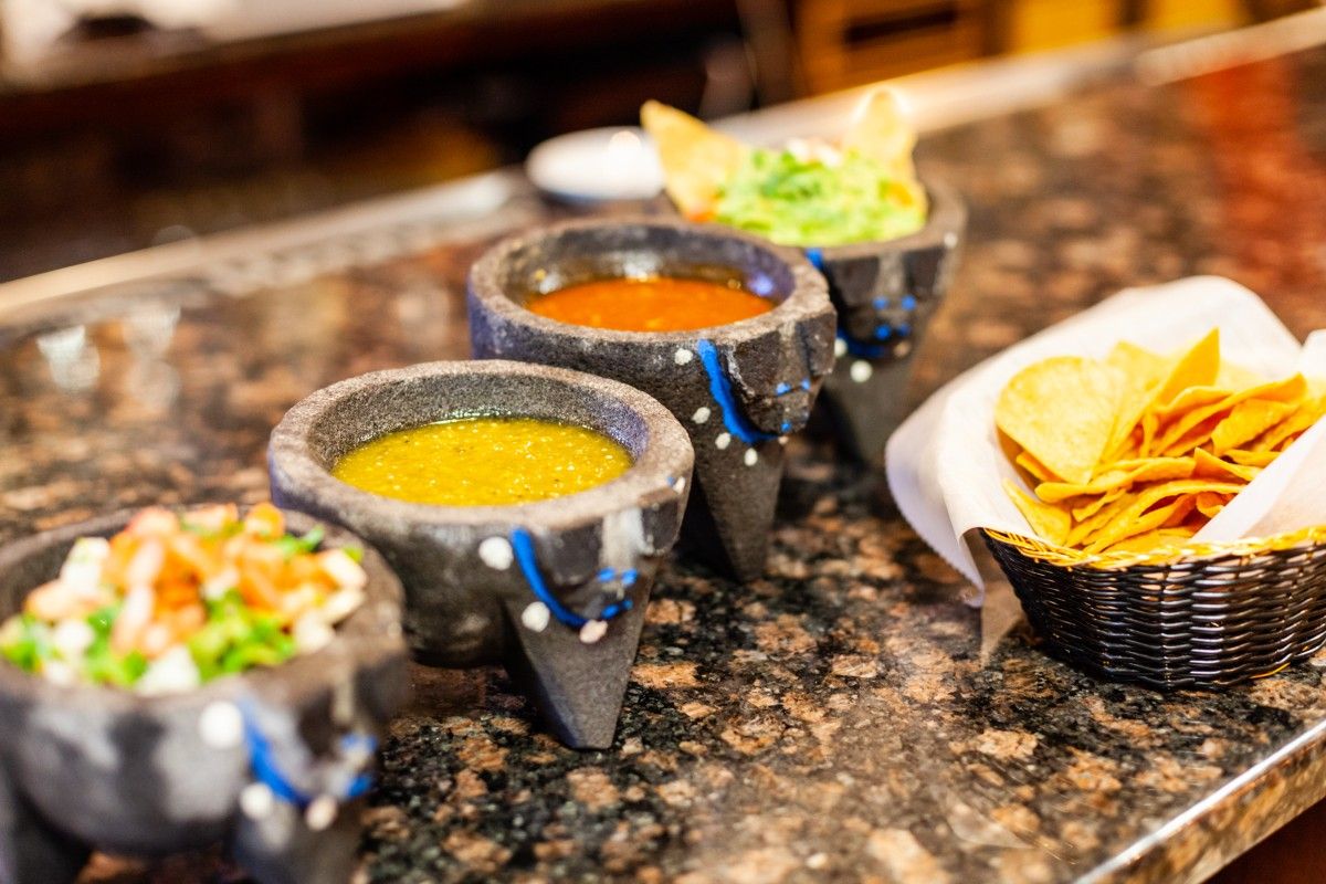 Bowls of salsa and guacamole with tortilla chips on a bar top.