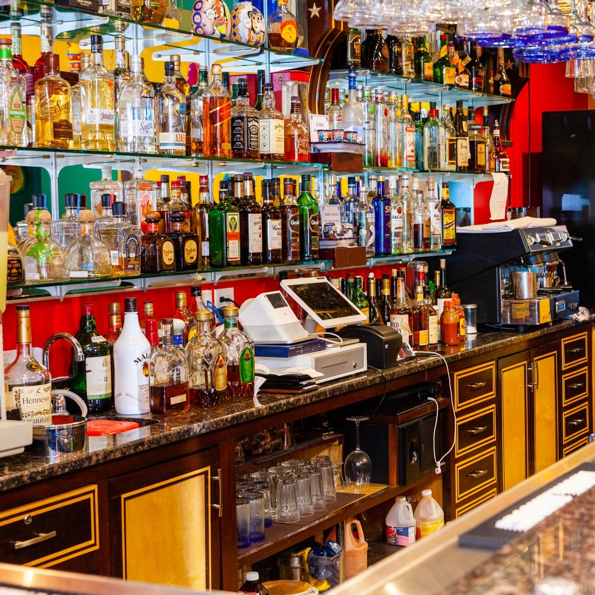 Bar interior with shelves of liquor bottles and bar equipment, including a cash register.
