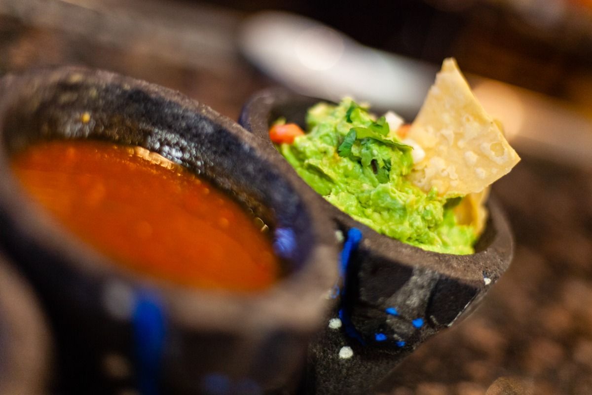 Close-up of salsa and guacamole in dark, stone bowls with a tortilla chip.