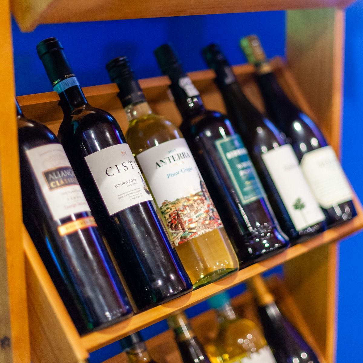 Wine bottles on a wooden rack, various labels, tilted against a blue background.