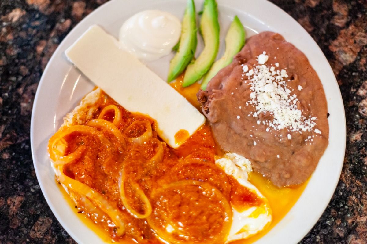 Plate of Mexican breakfast with eggs, beans, cheese, avocado, and sauce.