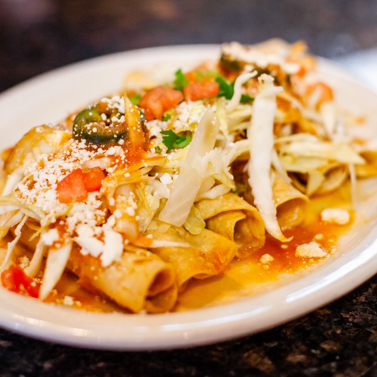 Plate of enchiladas topped with shredded cabbage, tomatoes, cheese, jalapeños, and sauce.