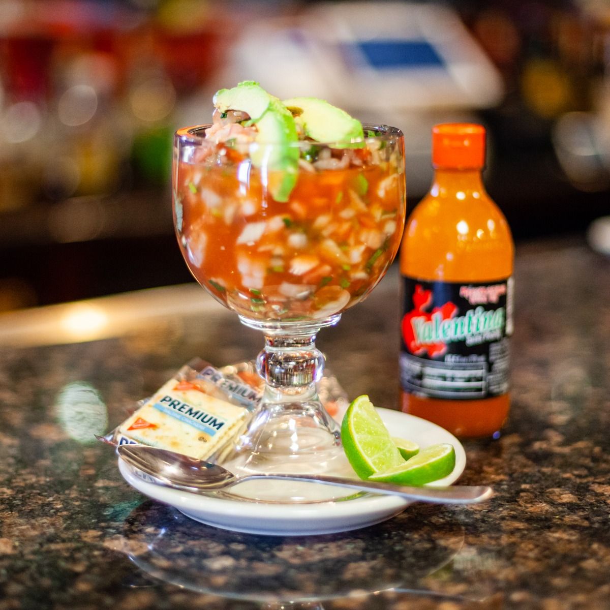 Seafood ceviche in a stemmed glass, with crackers, lime, and hot sauce on a bar.