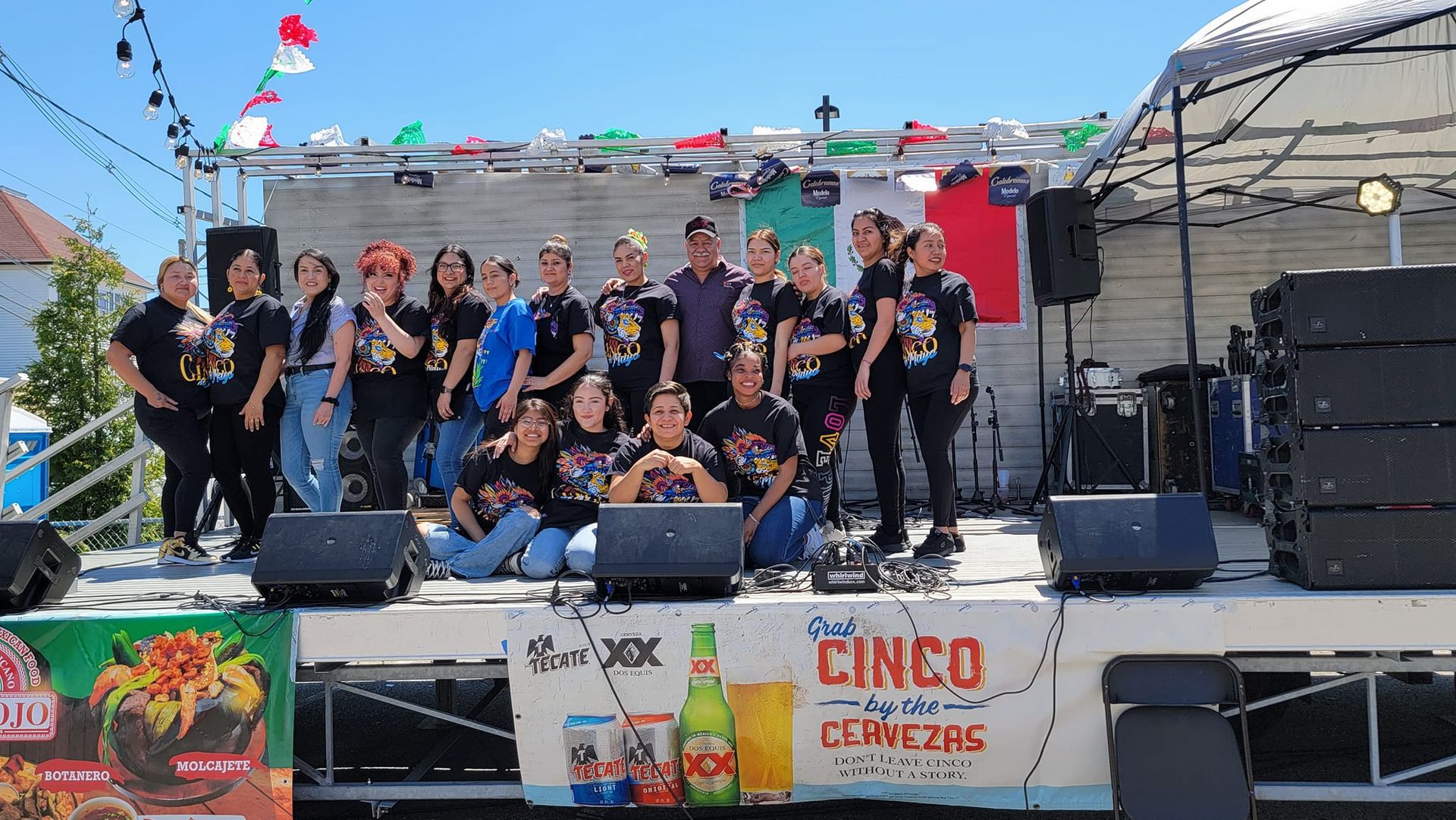 A group of people posing on a stage, banners and flags for Cinco De Mayo event.