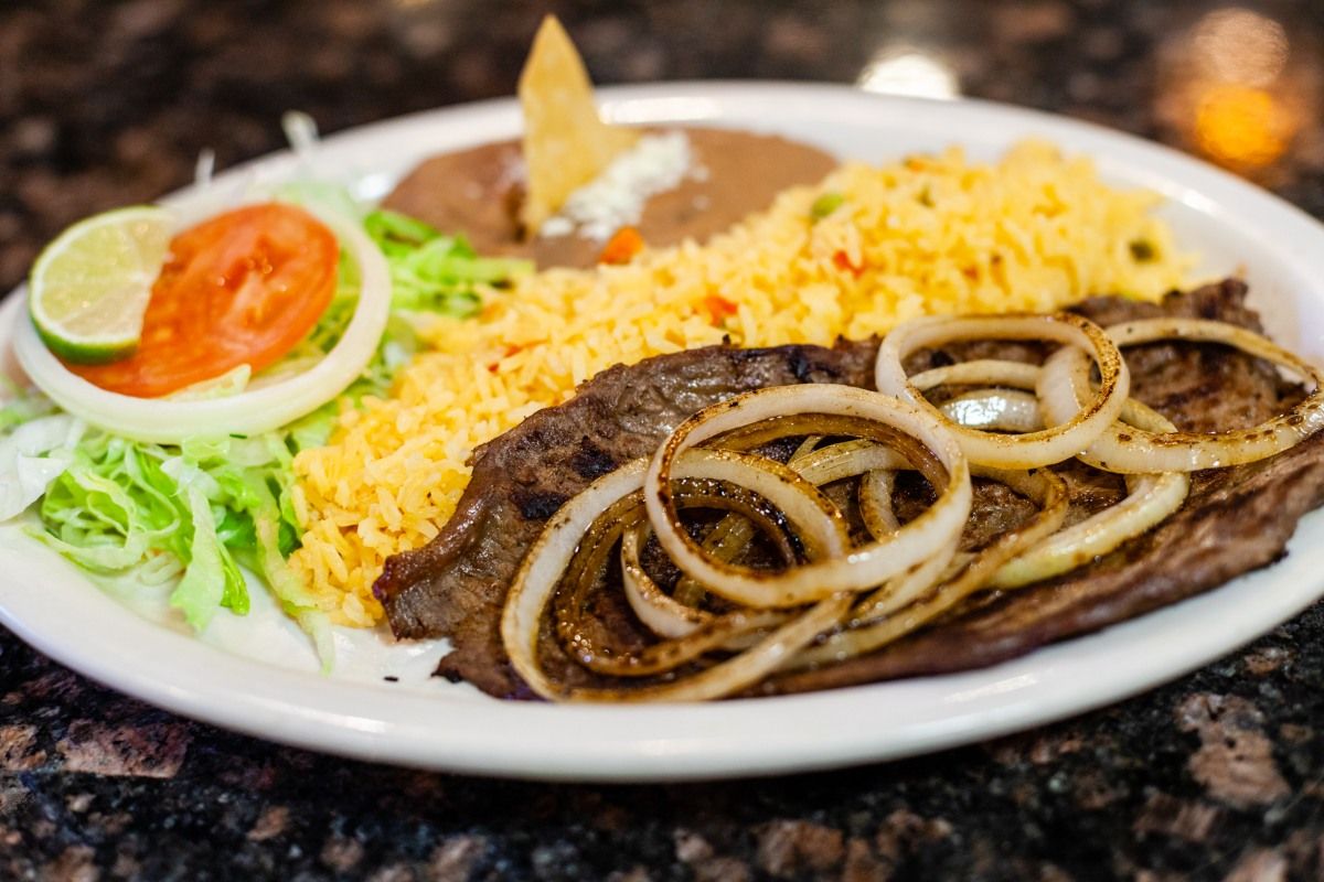 Steak plate with rice, beans, lettuce, tomato, onion, and lime.