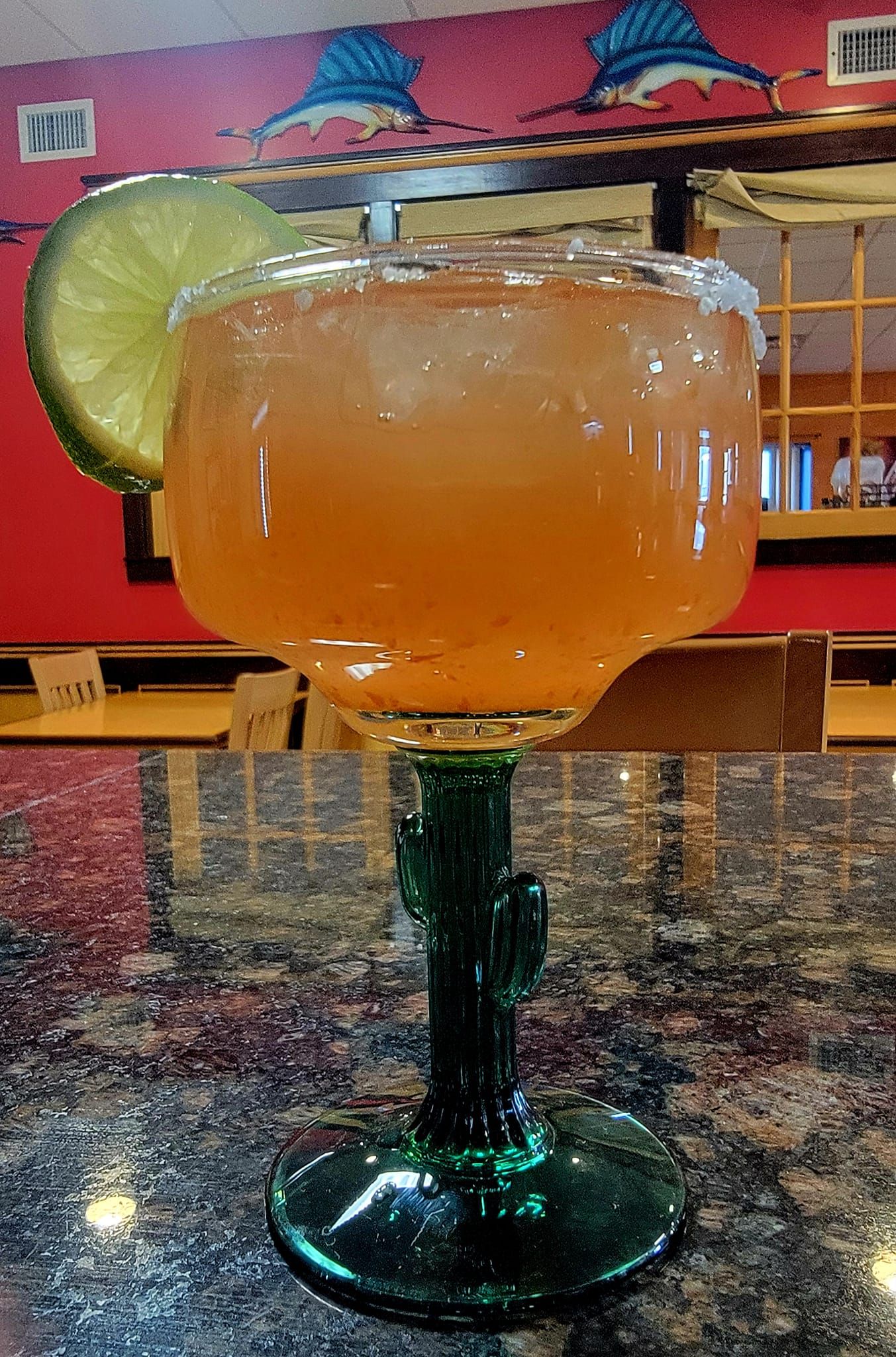 Margarita in a green cactus glass, lime garnish, on a table. Restaurant background.