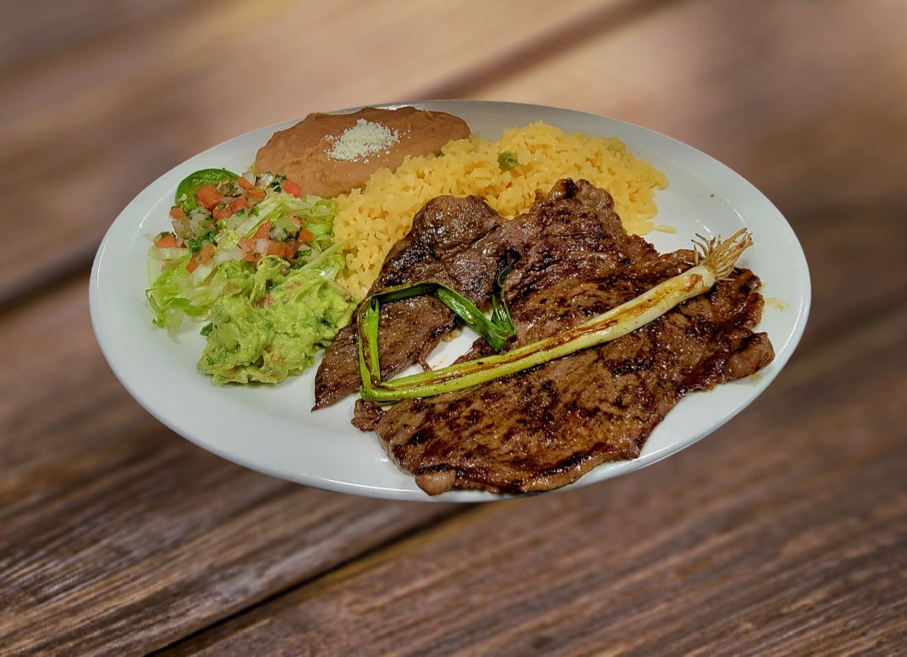 Grilled steak with rice, beans, and guacamole on a white plate.