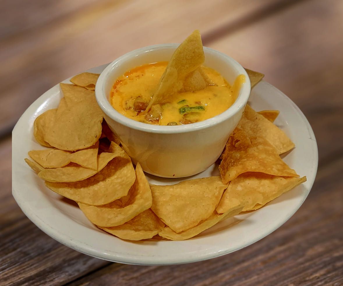 Cheese dip in a white bowl, surrounded by tortilla chips on a white plate.