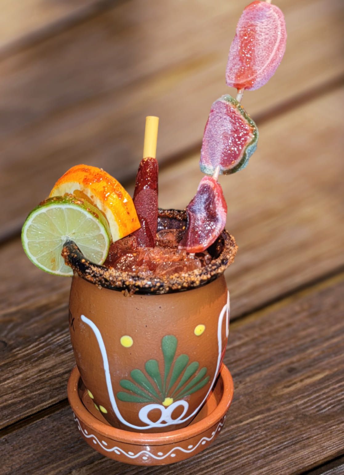 Clay mug cocktail, rimmed with seasoning, garnished with fruit and candies.