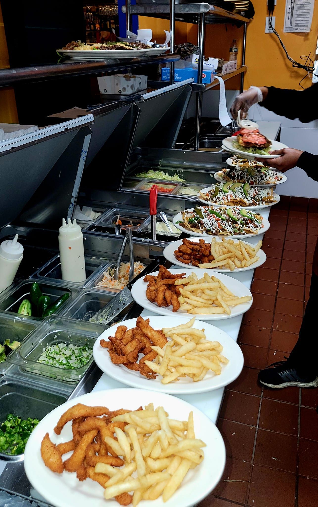 Plates of food stacked high on a counter at a restaurant, being served by a person.