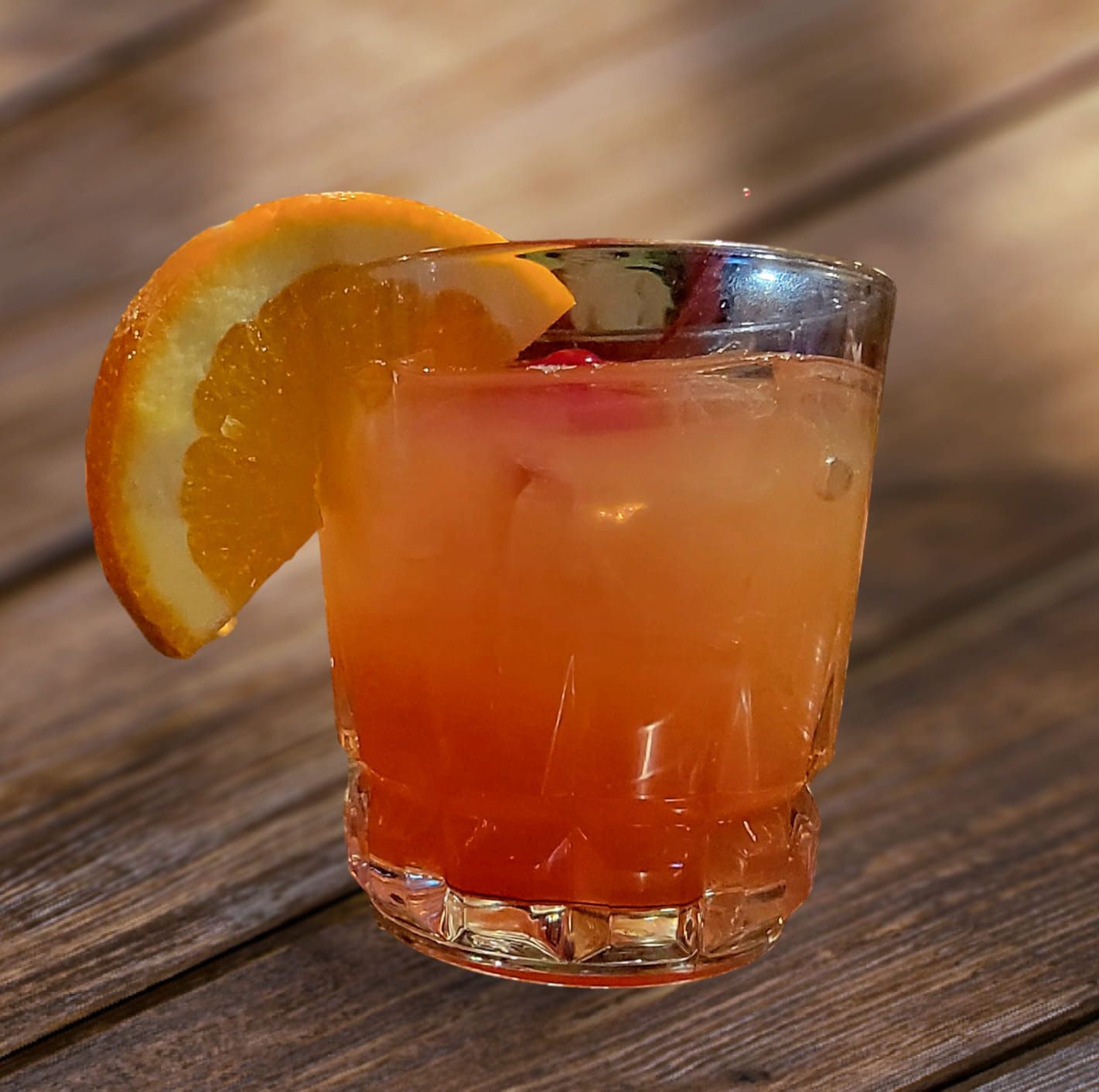 Cocktail in a glass with orange slice garnish, on a wooden surface.