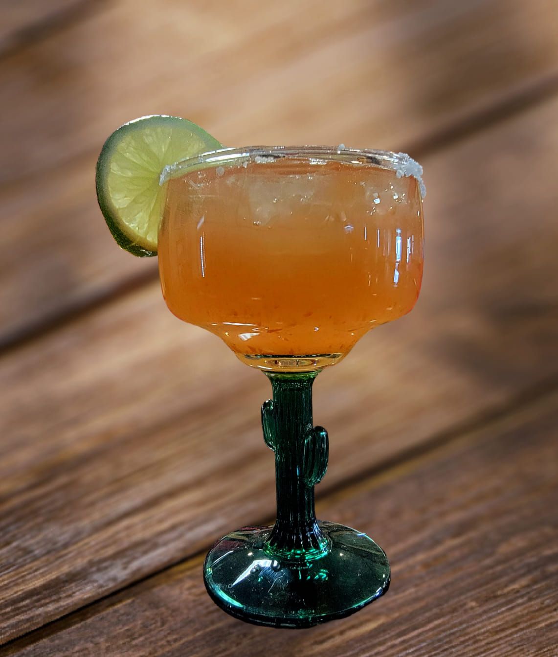 Margarita in a cactus-stemmed glass with a lime slice, salt rim, on a wooden table.