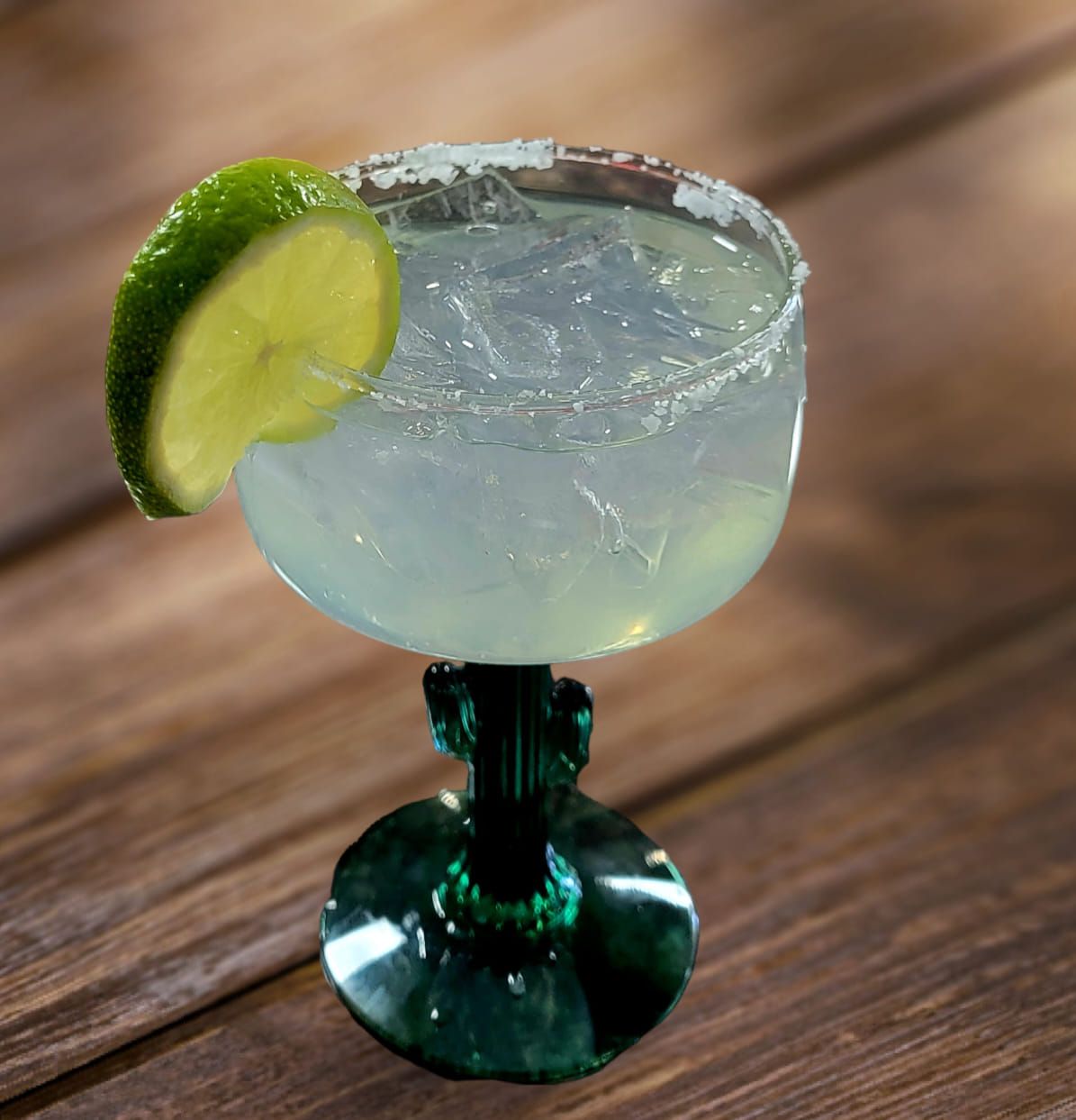 Margarita cocktail in a green stemmed glass, lime wedge garnish, salt rim, wooden background.