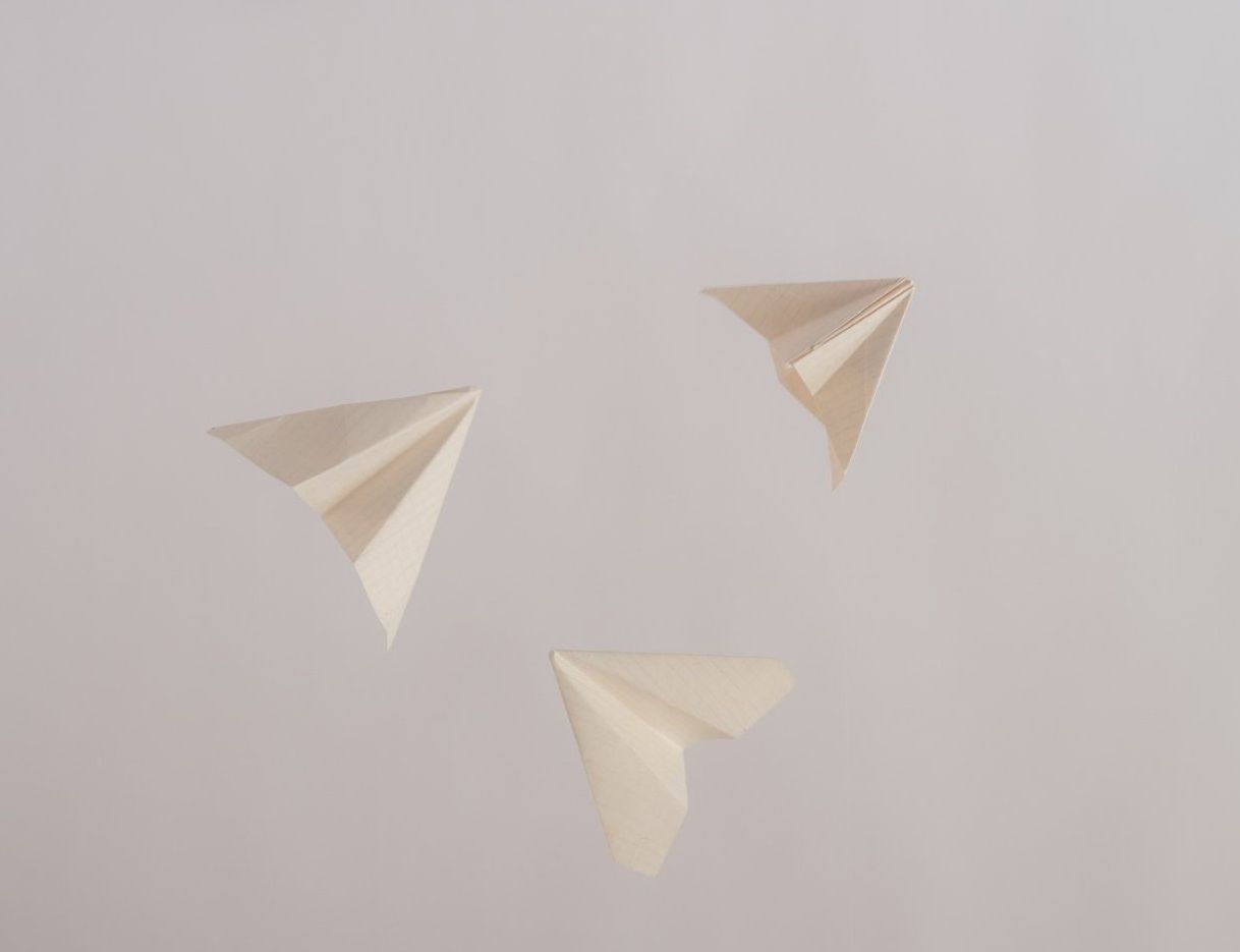 Three paper airplanes are flying in the air on a white background.