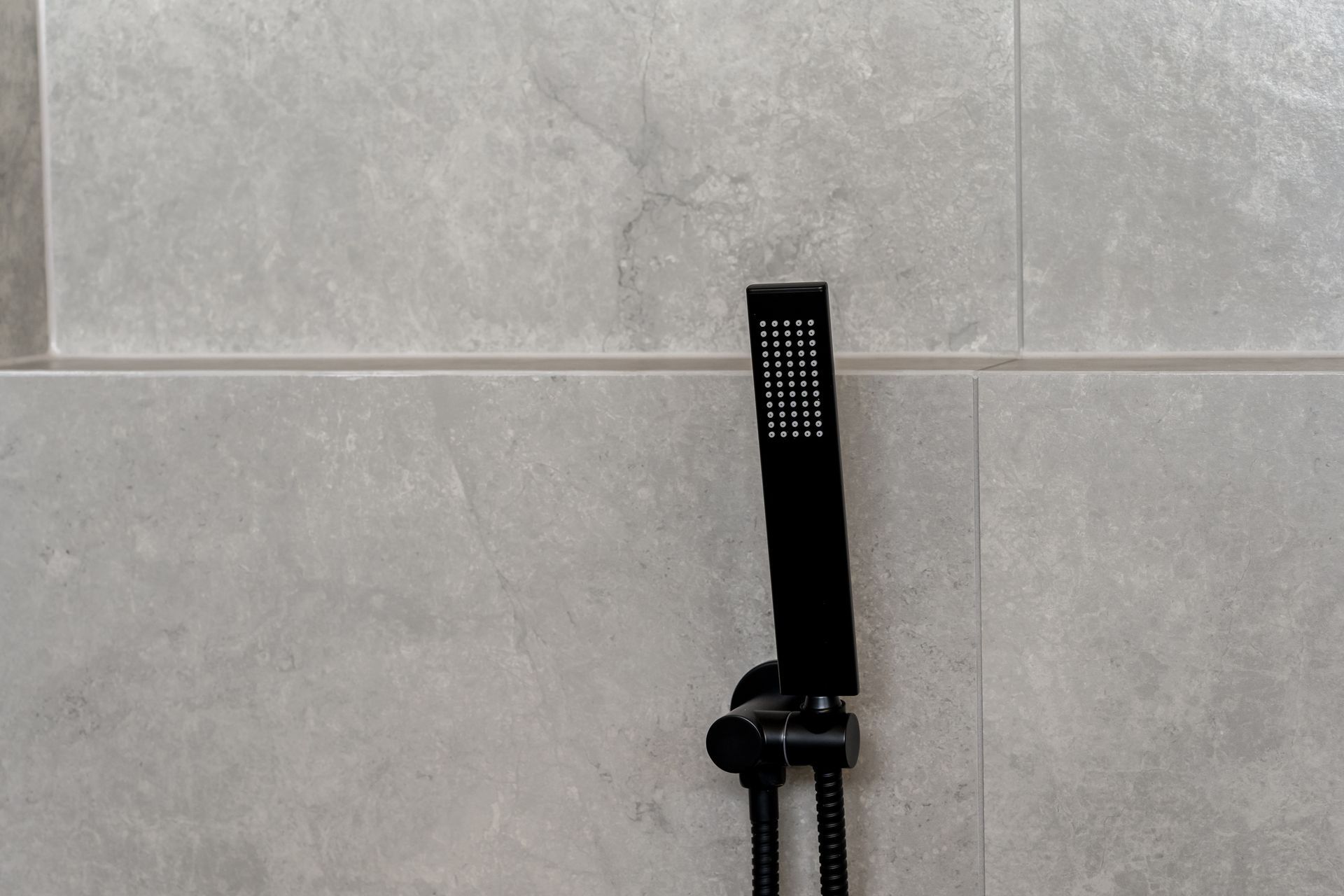 Black Handheld Showerhead Mounted on a Gray Tiled Bathroom Wall — Matt Made Building in Camden, NSW