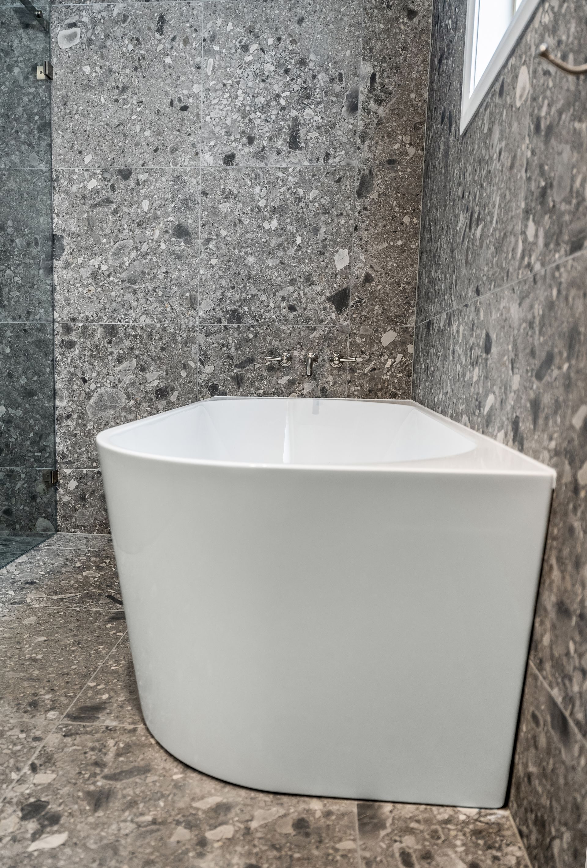 White Bathtub on a Stone Floor Against Textured Gray Walls, Viewed From Above — Matt Made Building in Camden, NSW