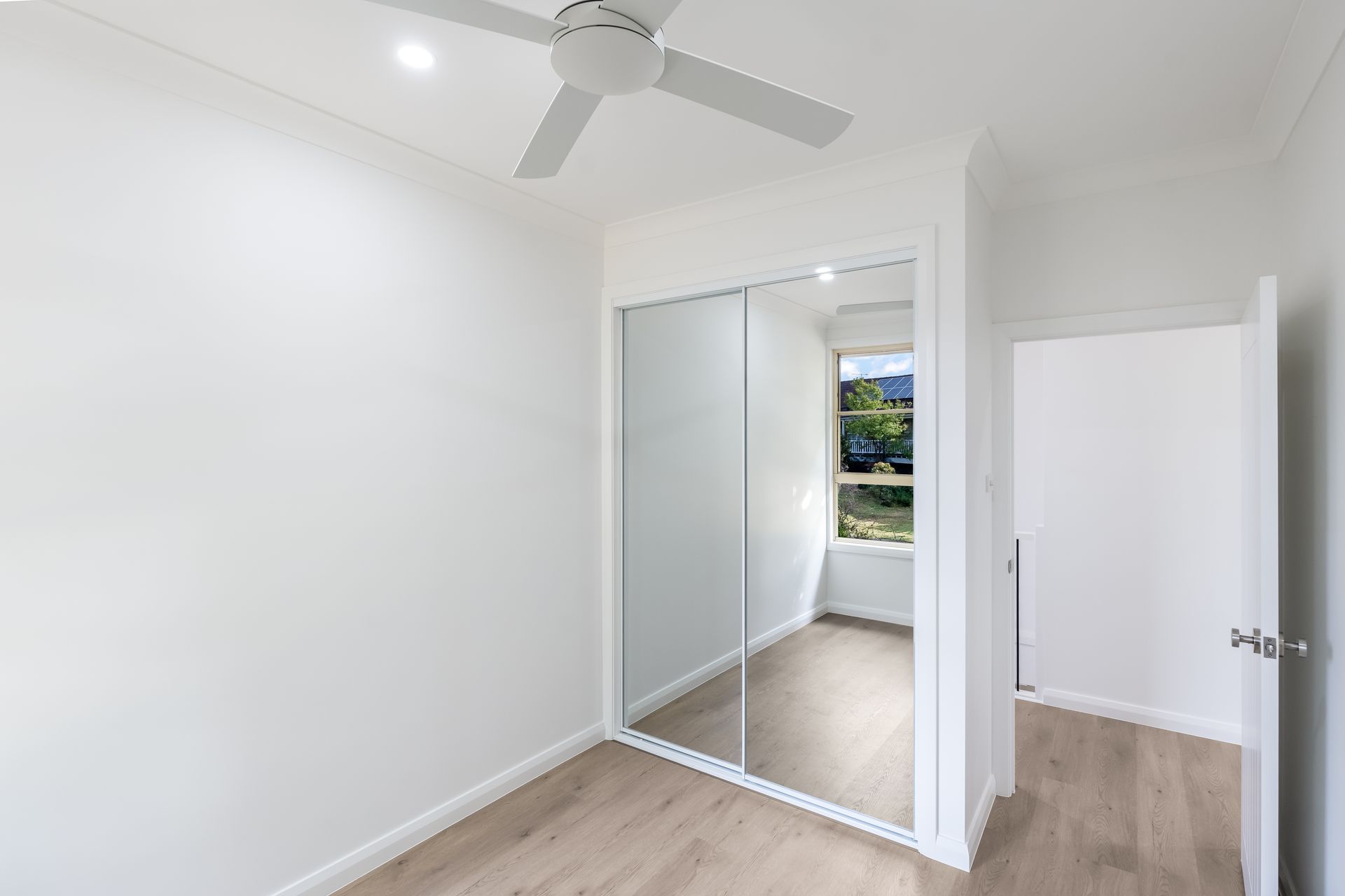 Empty White Bedroom With Mirrored Closet Doors and Window Light — Matt Made Building in Camden, NSW