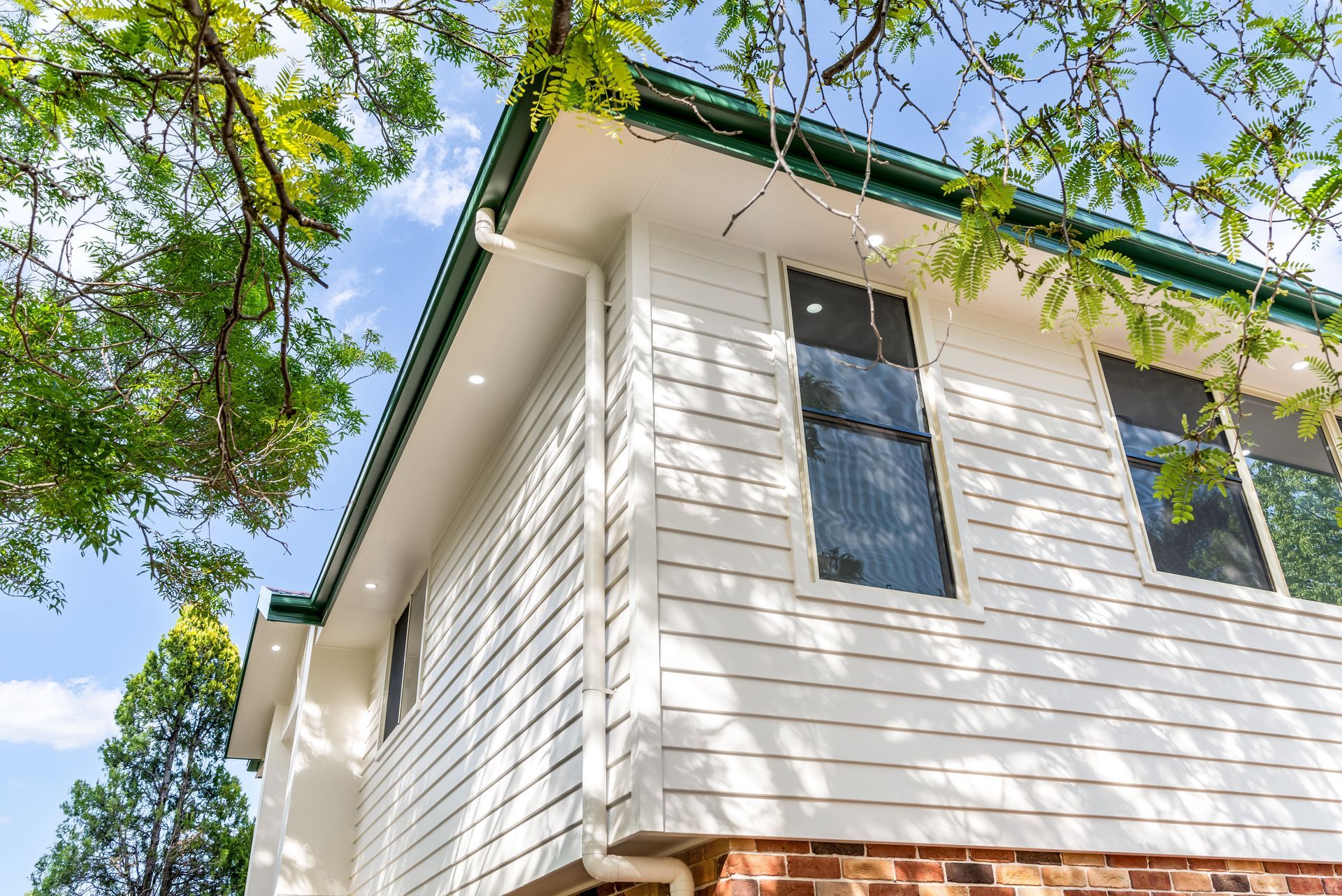 White Two-story House Exterior With Green Tree Branches and Blue Sky Above — Matt Made Building in Camden, NSW