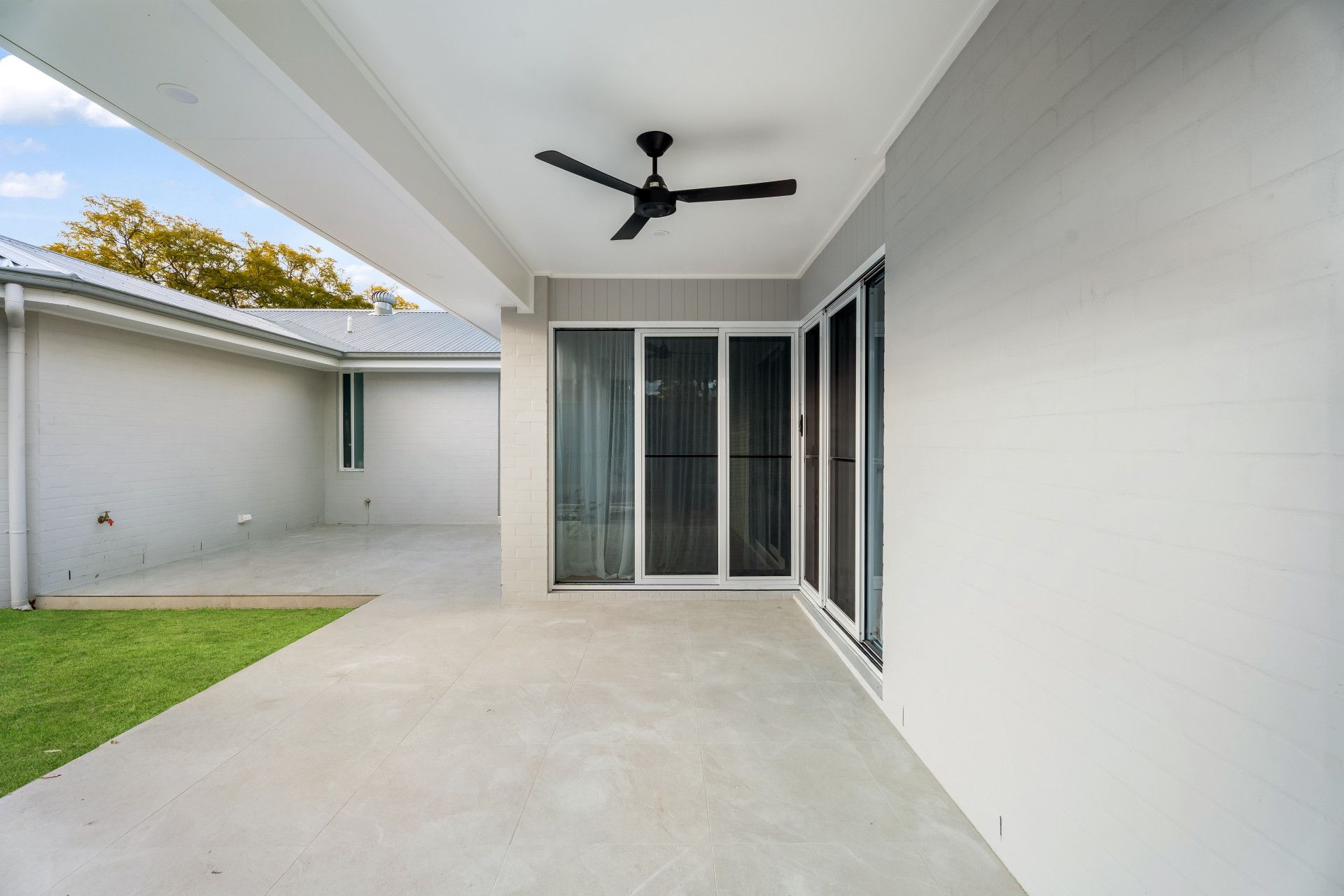 Covered patio with concrete floor, white walls, ceiling fan and sliding glass doors opening to a lawn - Matt Made Building - Builder Camden, NSW.