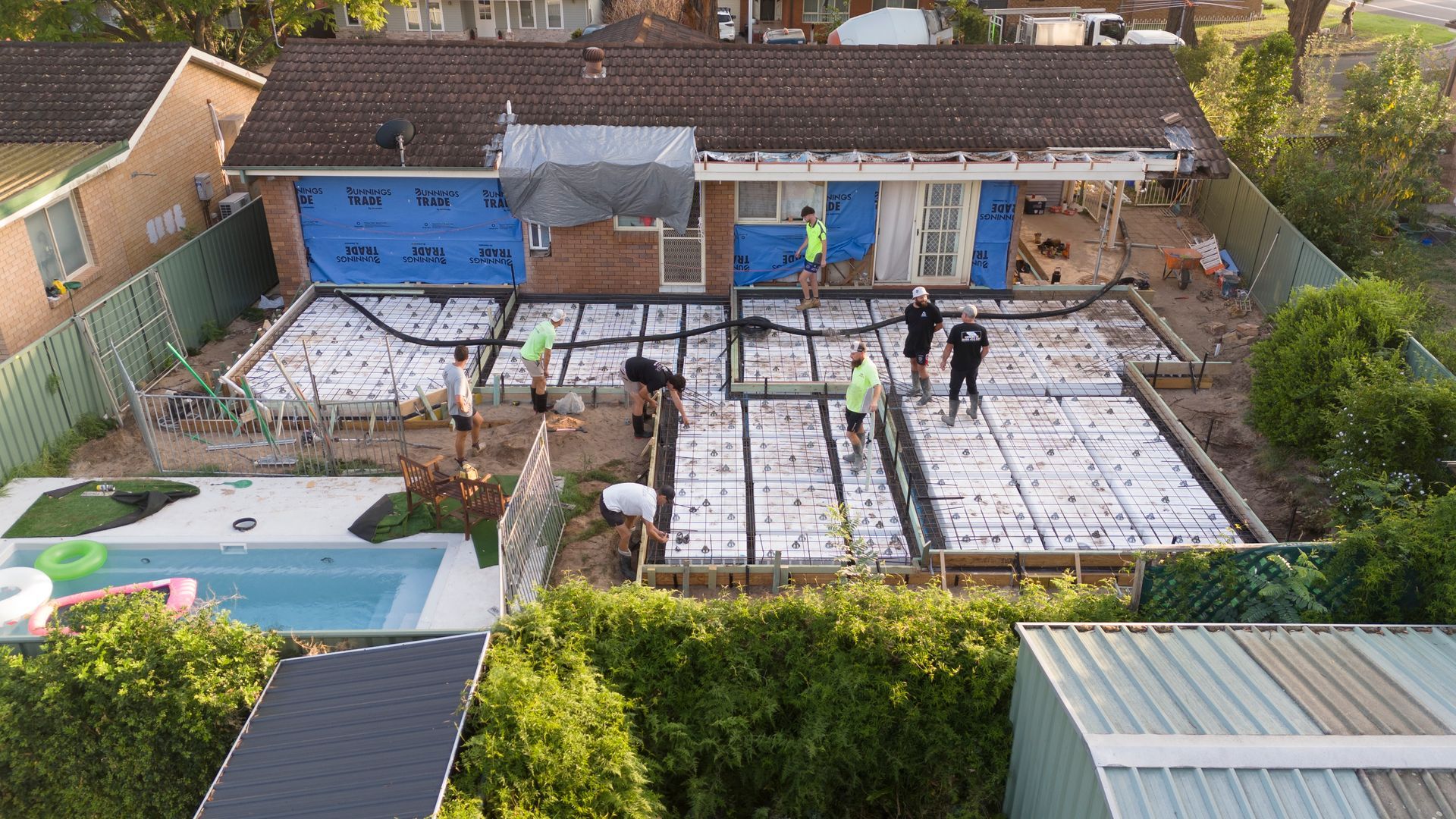 Backyard Renovation in Progress With Workers, Exposed Foundation, Blue House Facade — Matt Made Building in Camden, NSW