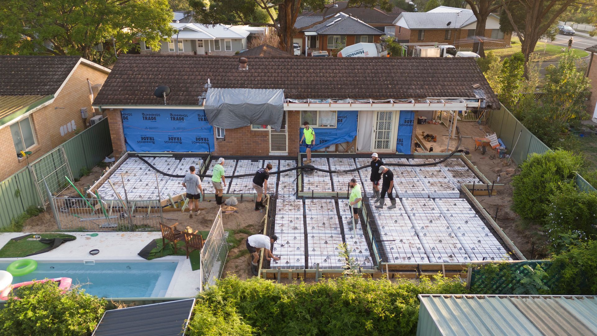 Workers Installing White Patio Pavers in a Backyard Beside a House and Pool — Matt Made Building in Camden, NSW