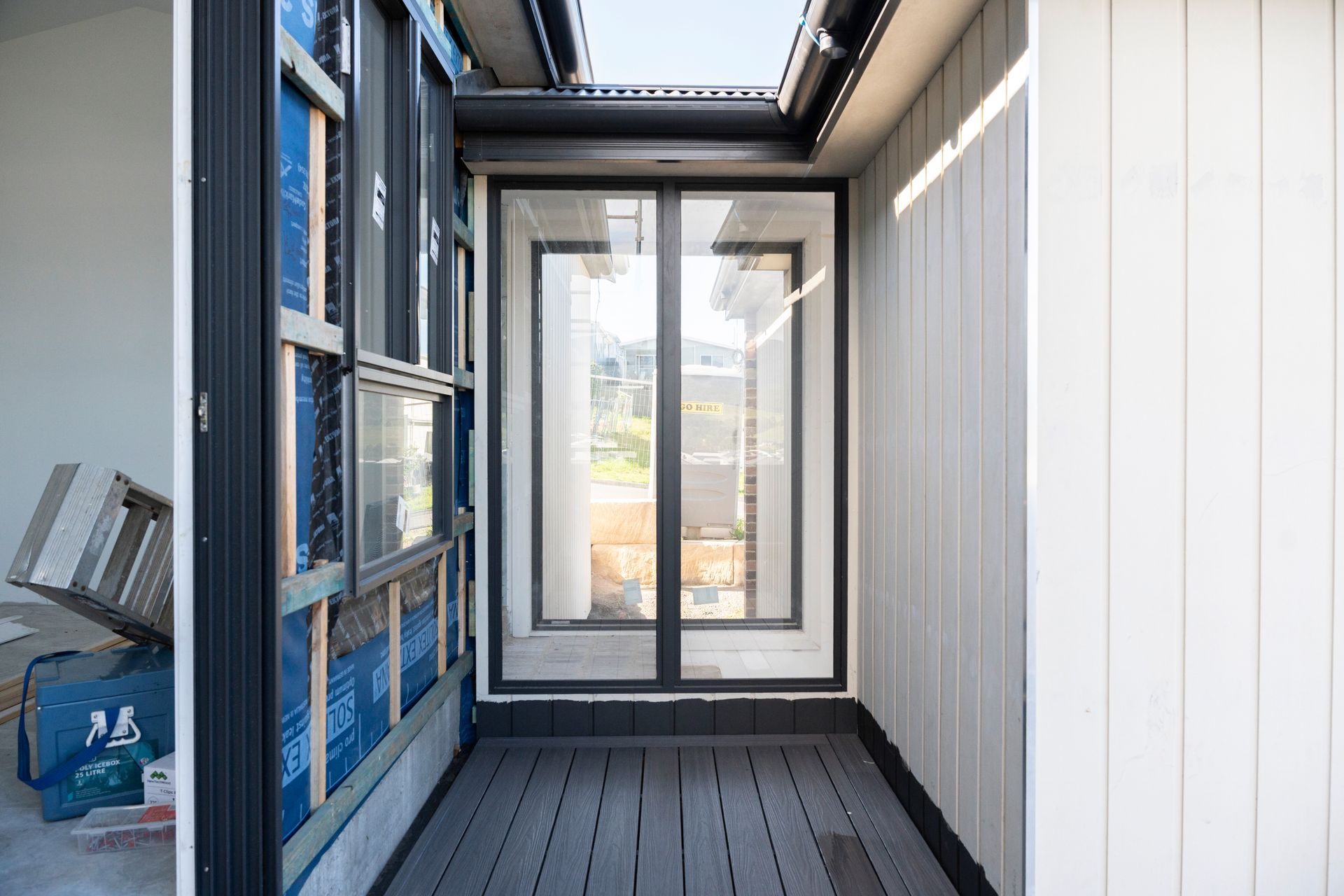 Narrow Porch With Gray Deck, Glass Door, Blue Shelving, and White Siding — Matt Made Building in Camden, NSW