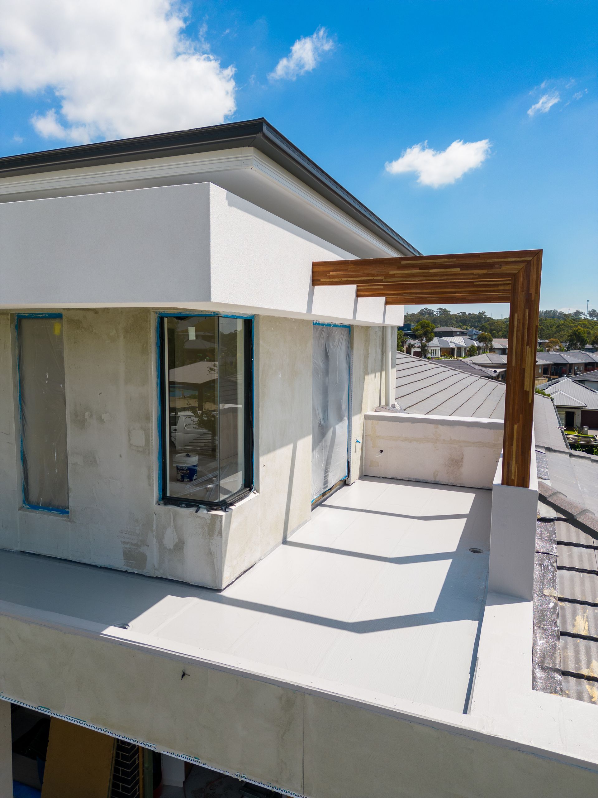 Modern White Rooftop Patio With Glass Railing, Wooden Pergola, and Blue Sky — Matt Made Building in Camden, NSW