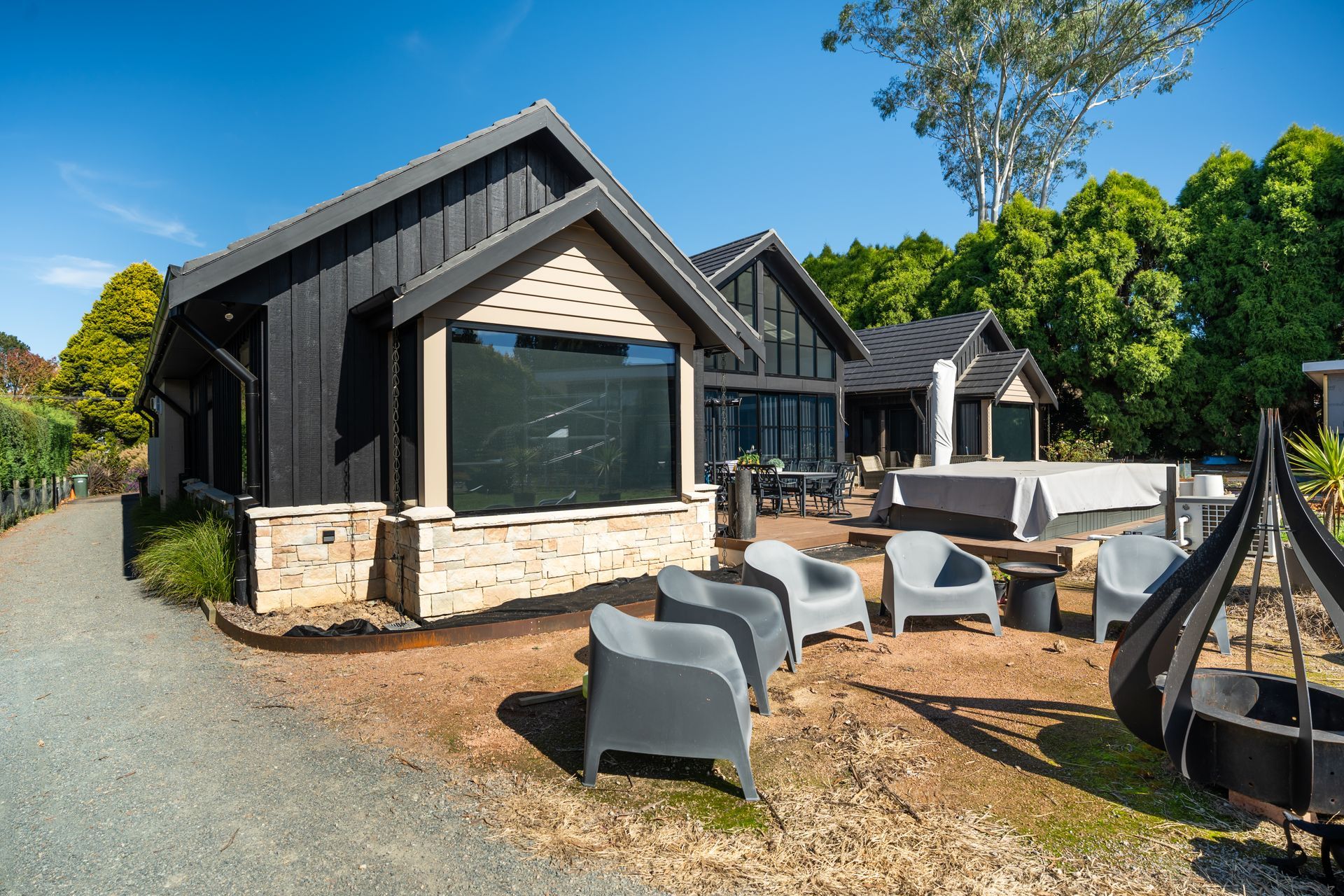 Modern Black Cabin With Outdoor Patio Seating and Fire Pit on a Sunny Day — Matt Made Building in Camden, NSW