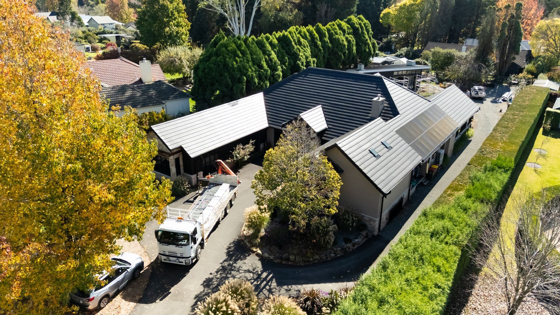 Aerial View of a House With Dark Roof and Autumn Trees Beside a Road and Hillside — Matt Made Building in Camden, NSW