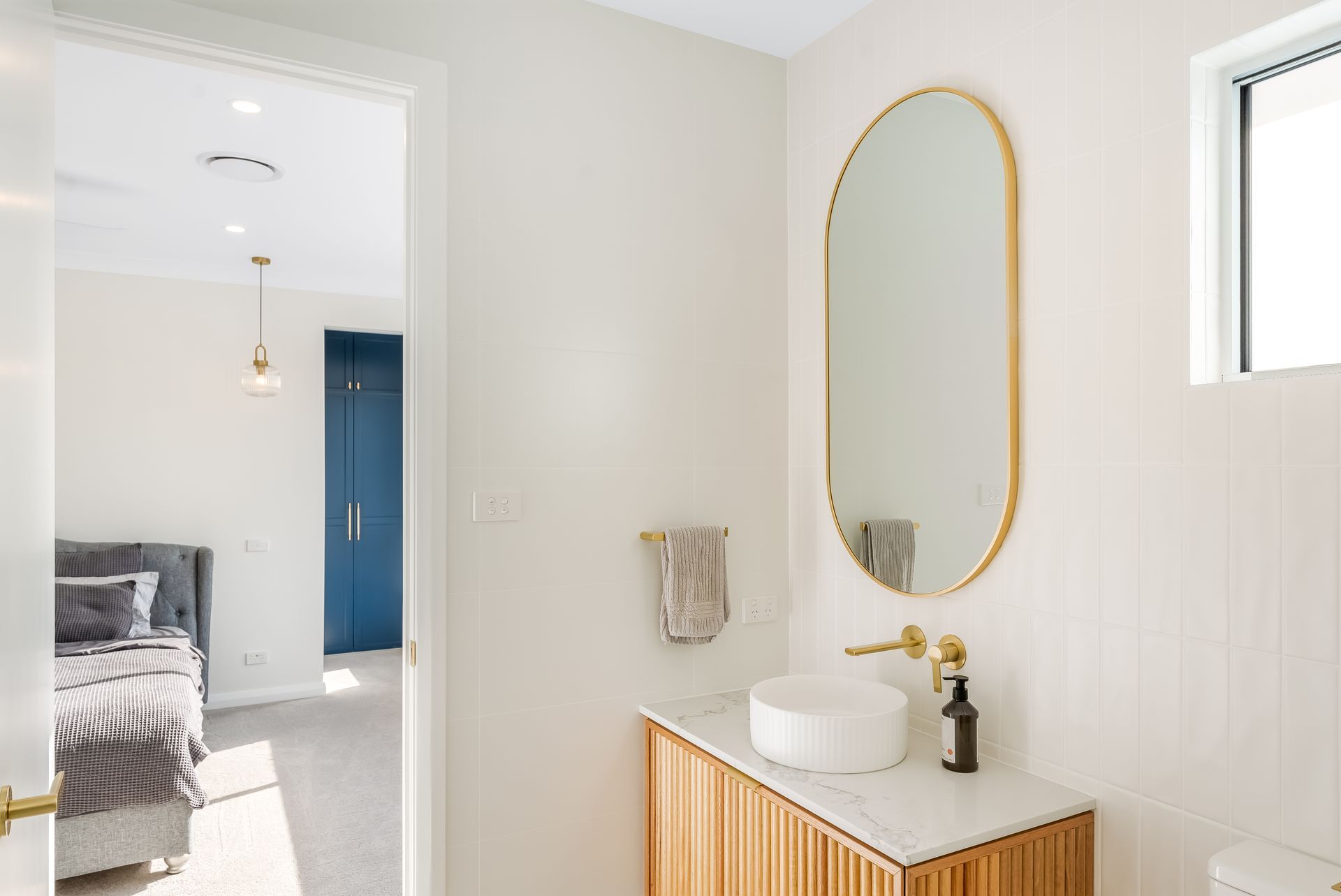 Bright Bathroom Vanity With Gold Oval Mirror and Towel Beside a Bedroom Doorway — Matt Made Building in Camden, NSW