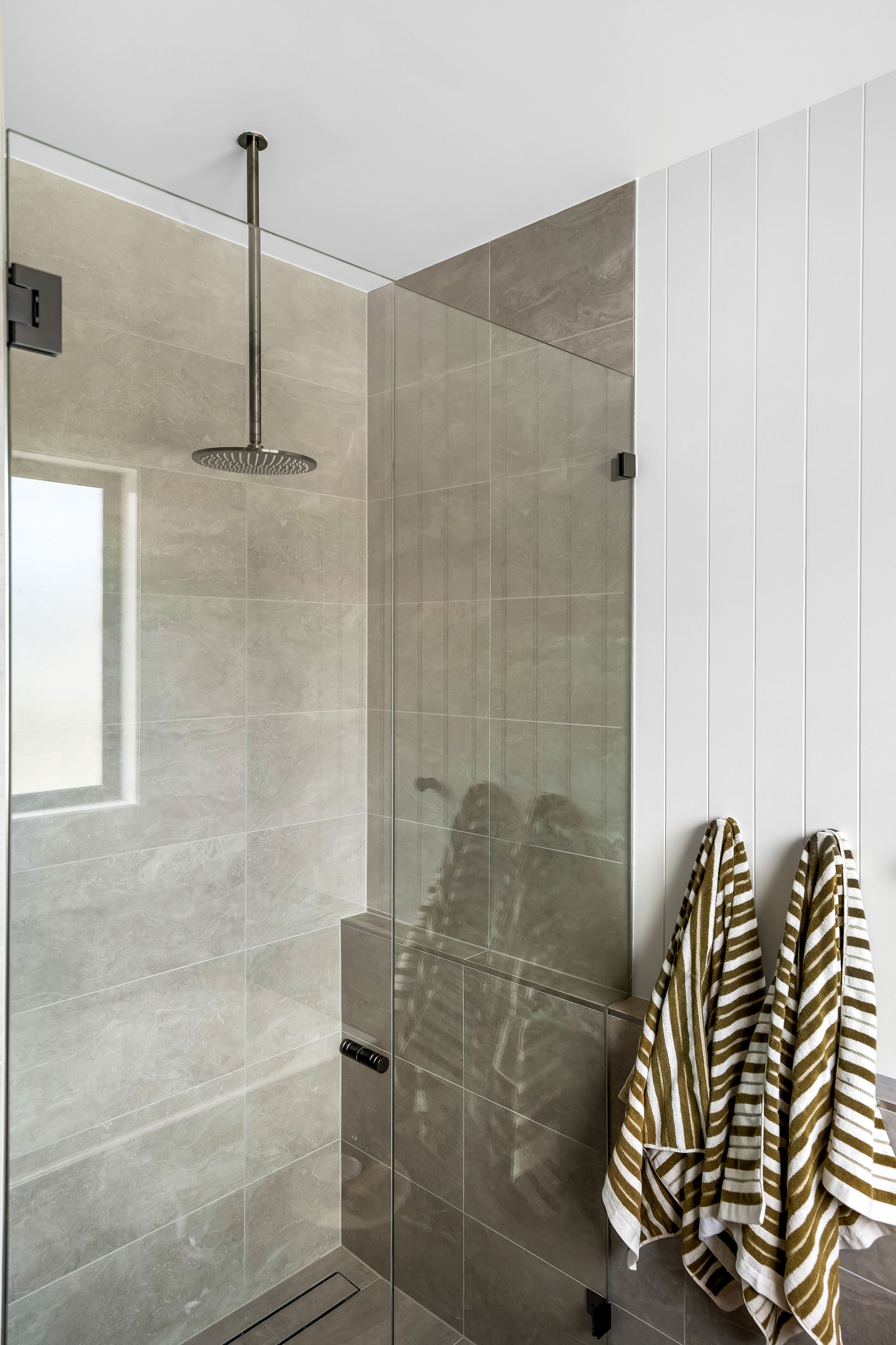 Modern Shower With Glass Partition and Striped Towels Hanging on the Wall — Matt Made Building in Camden, NSW