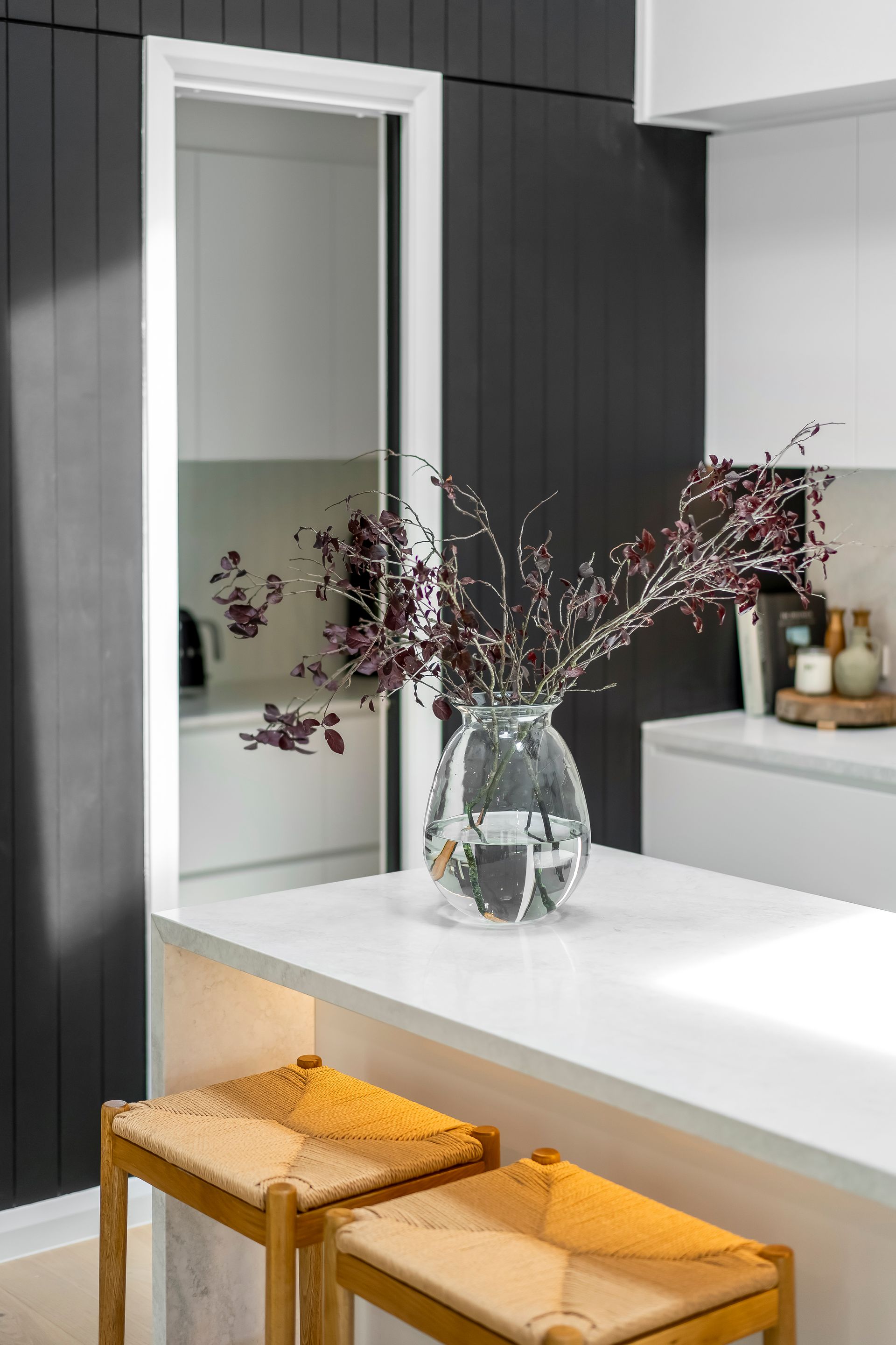 Modern Kitchen With White Island and Two Woven Stools by a Mirror Wall — Matt Made Building in Camden, NSW
