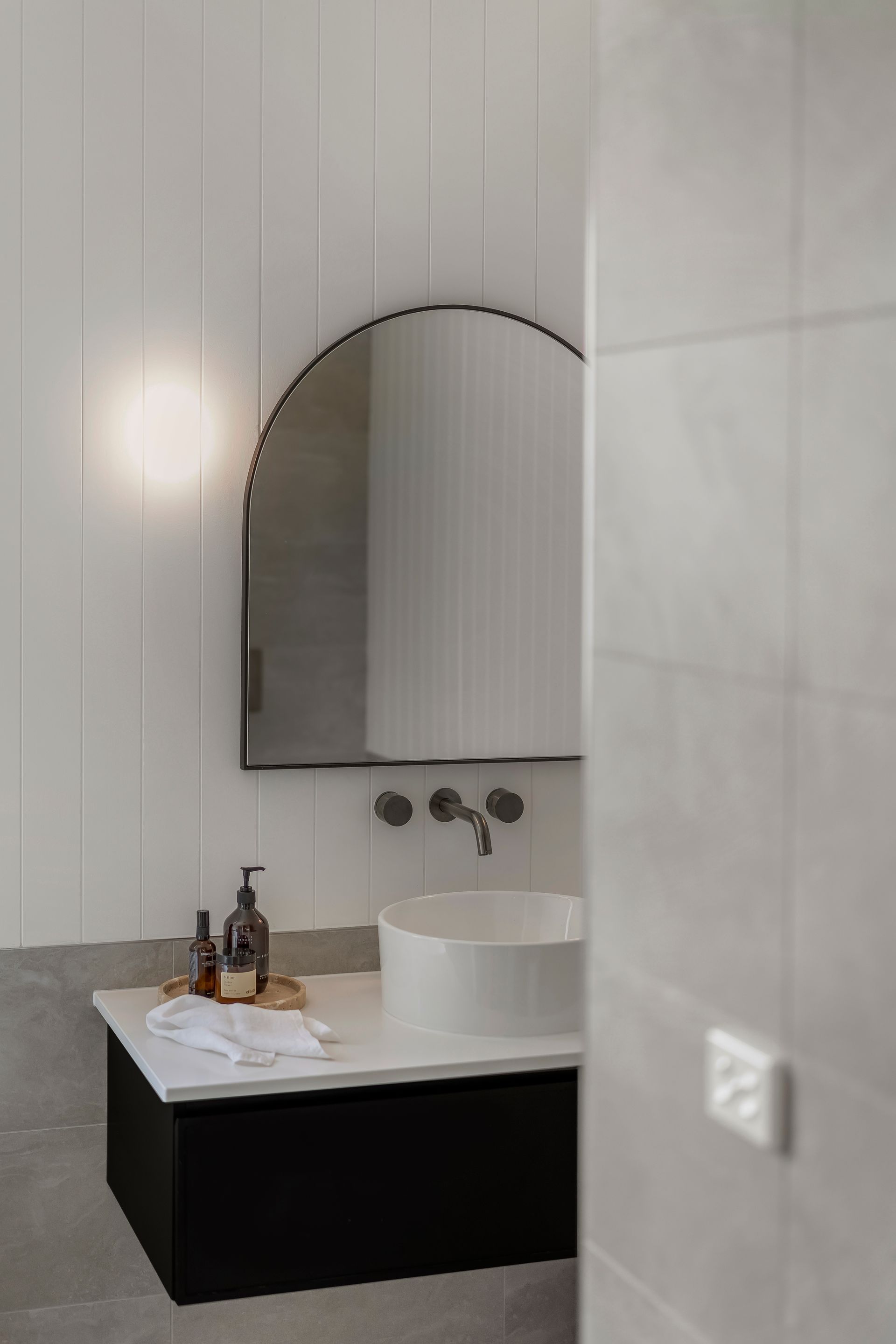 Modern Bathroom Vanity With Arched Mirror and Black Cabinet Against Light  — Matt Made Building in Camden, NSW