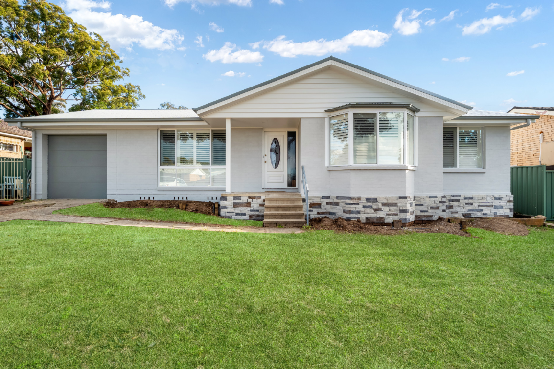 White single-story house with grey garage, front porch, and green lawn under a blue sky - Matt Made Building - Builder Camden, NSW.