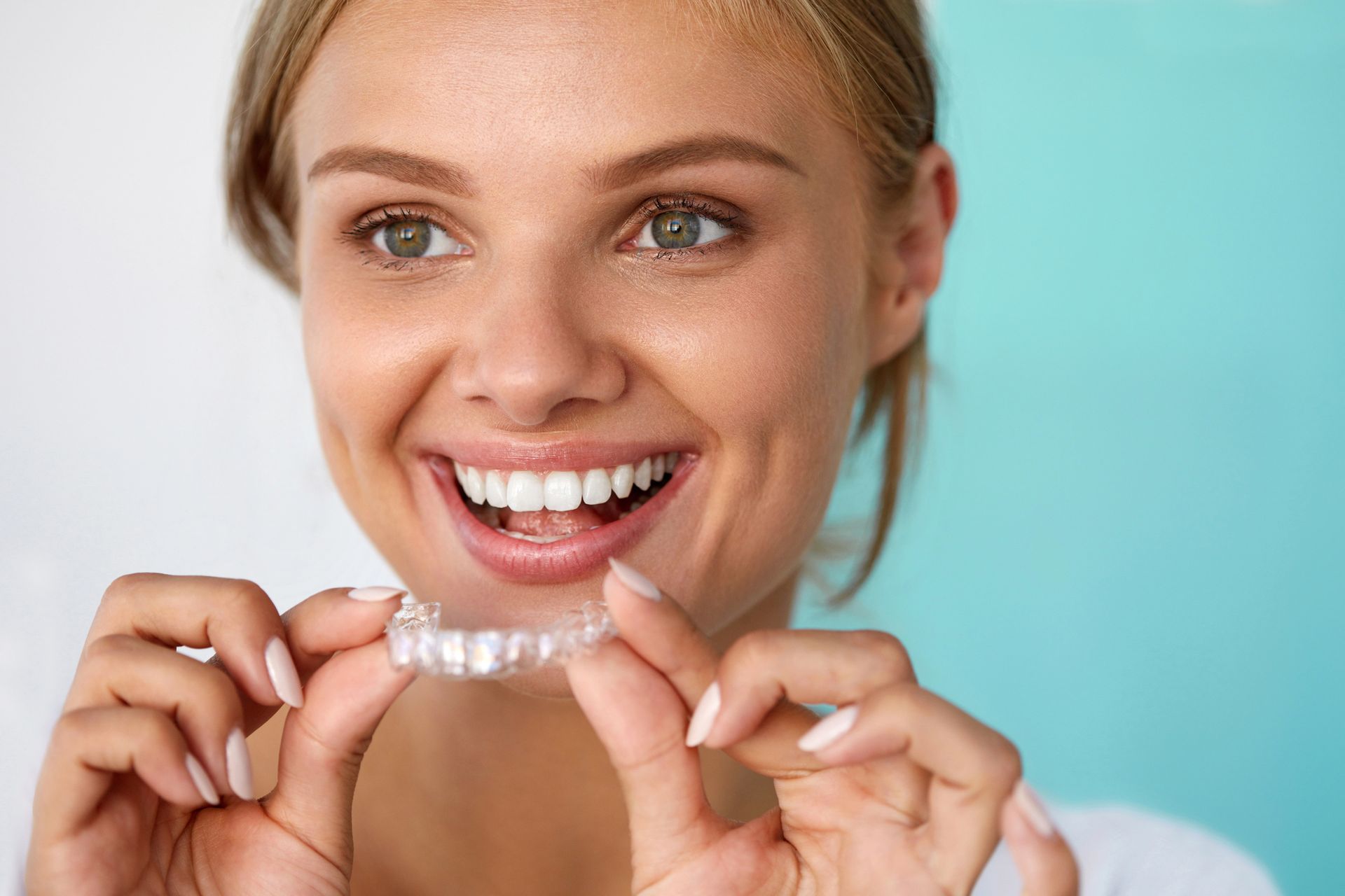 Persona sonriente sosteniendo alineadores dentales transparentes sobre un fondo turquesa.