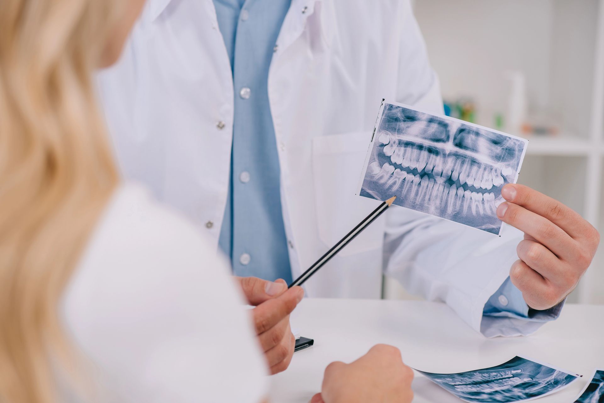 Dentista con bata blanca mostrando radiografías dentales a un paciente en una clínica.