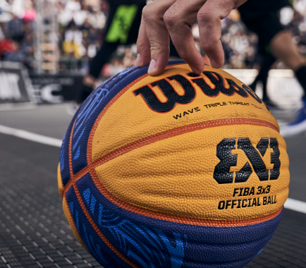 Hand holding a Wilson FIBA 3x3 basketball on a court; orange, blue, and black details.
