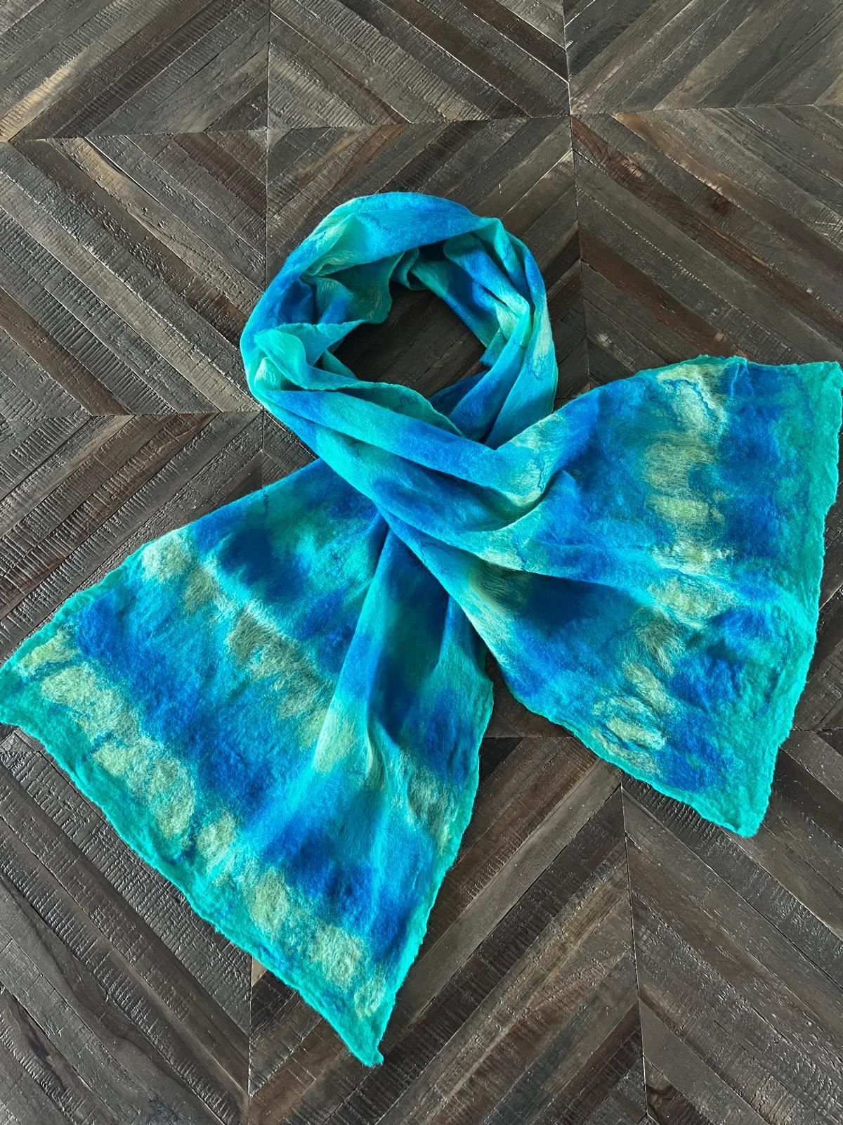 Een blauw-turquoise tie-dye sjaal op een donkere, bewerkte houten ondergrond.