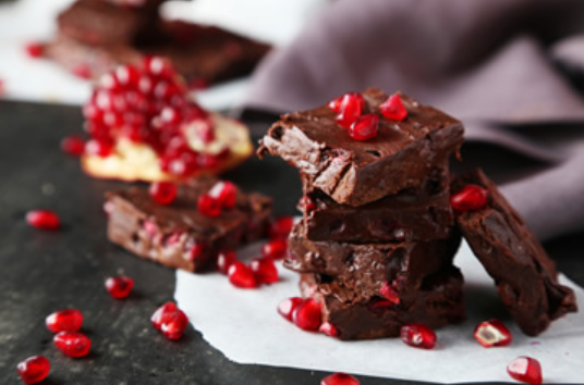 Chocoladebrownies met granaatappelpitjes erop, gestapeld op bakpapier.