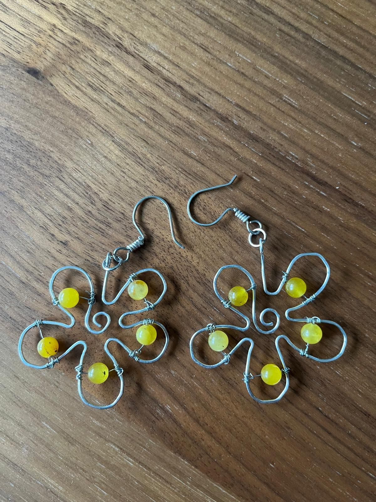 Een paar zilverkleurige en gele bloemvormige oorbellen op een houten ondergrond.