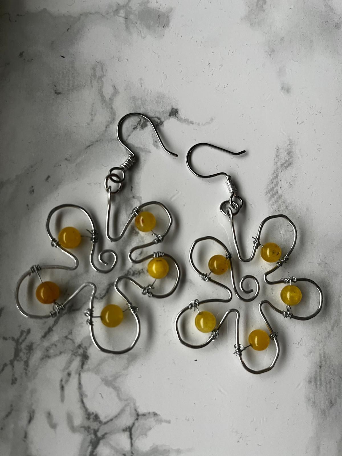 Een paar zilverkleurige en gele bloemvormige oorbellen op een houten ondergrond.