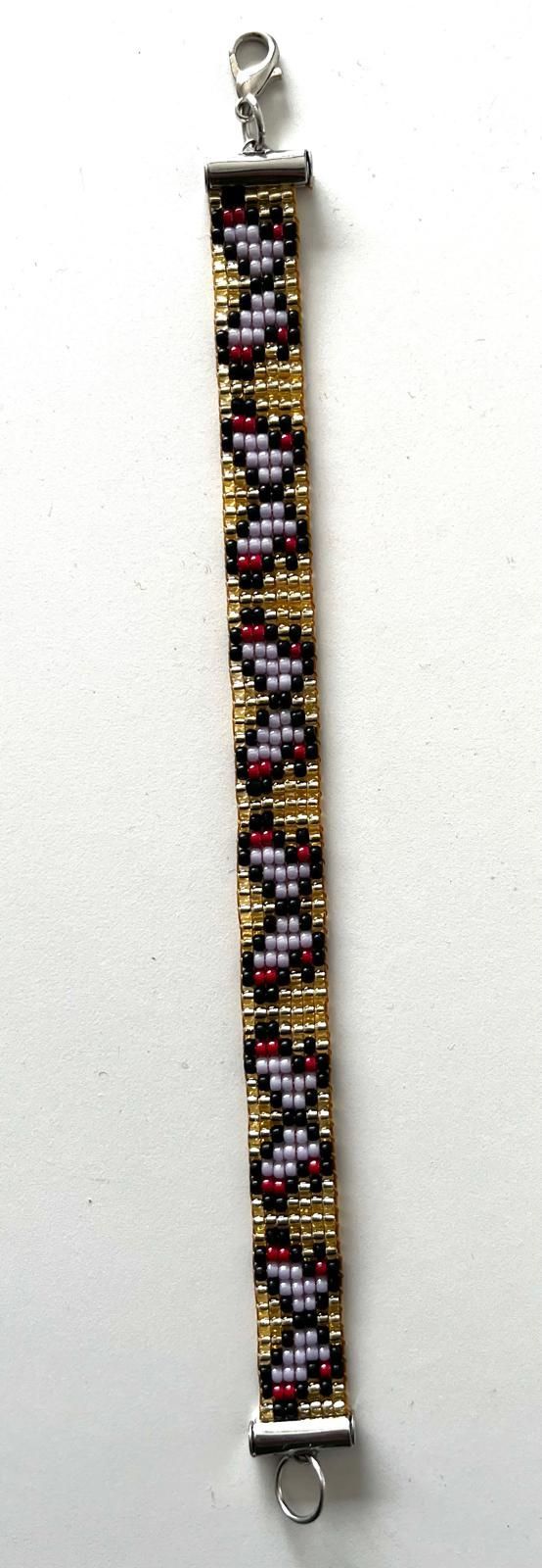 Kralenarmband met een bloemenpatroon in goud, zwart, wit en roze op een witte achtergrond.