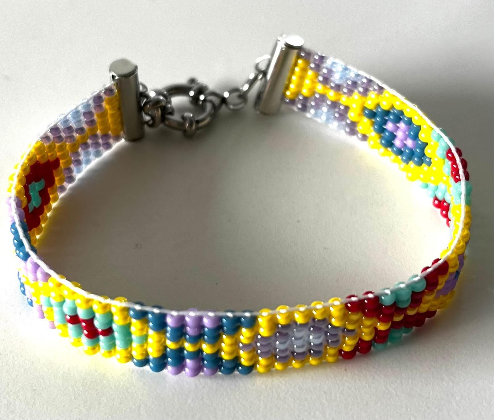 Kleurrijke kralenarmband met gele, blauwe, rode en witte patronen en een zilveren sluiting op een witte achtergrond.
