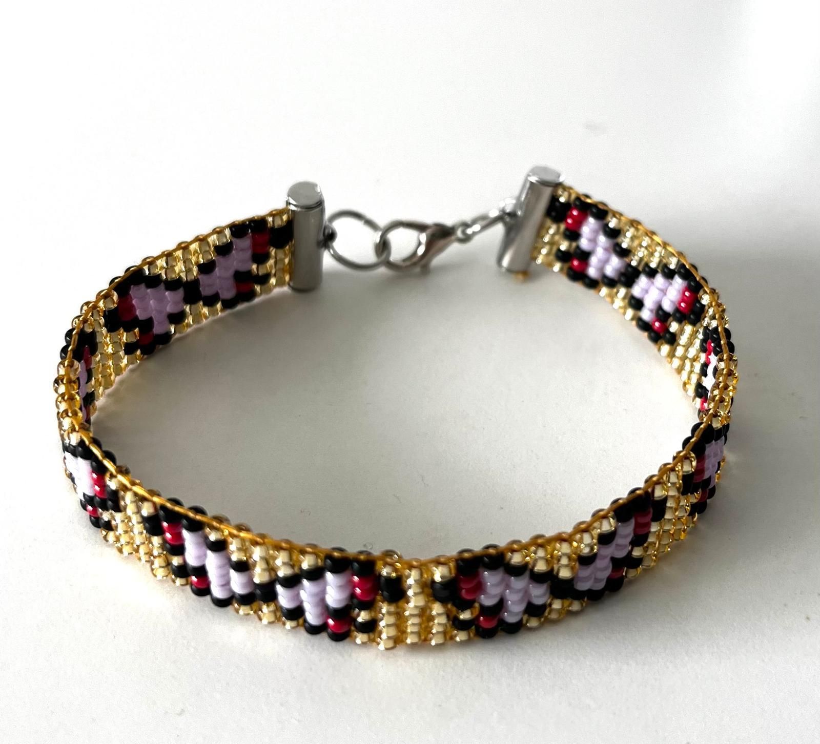 Kralenarmband met een bloemenpatroon in goud, zwart, wit en roze op een witte achtergrond.