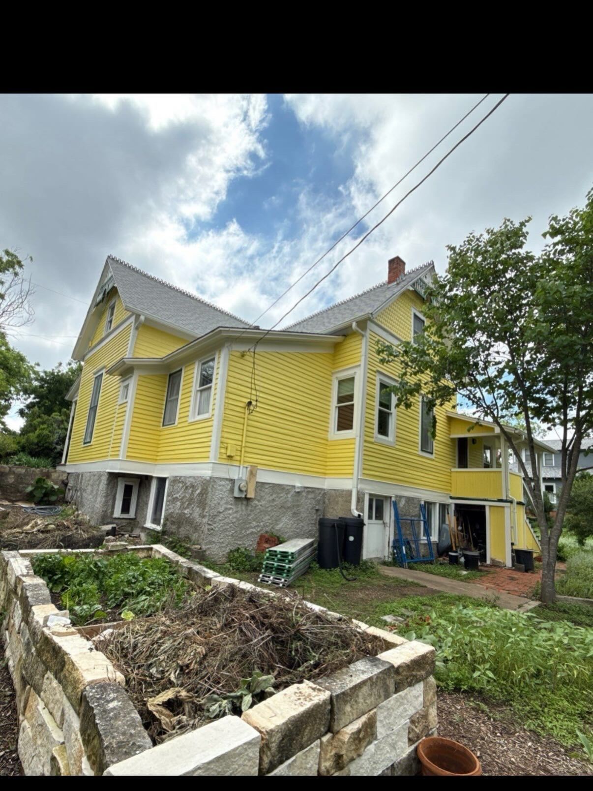 Yellow two-story house with white trim and stone foundation, viewed from a yard under a cloudy sky.