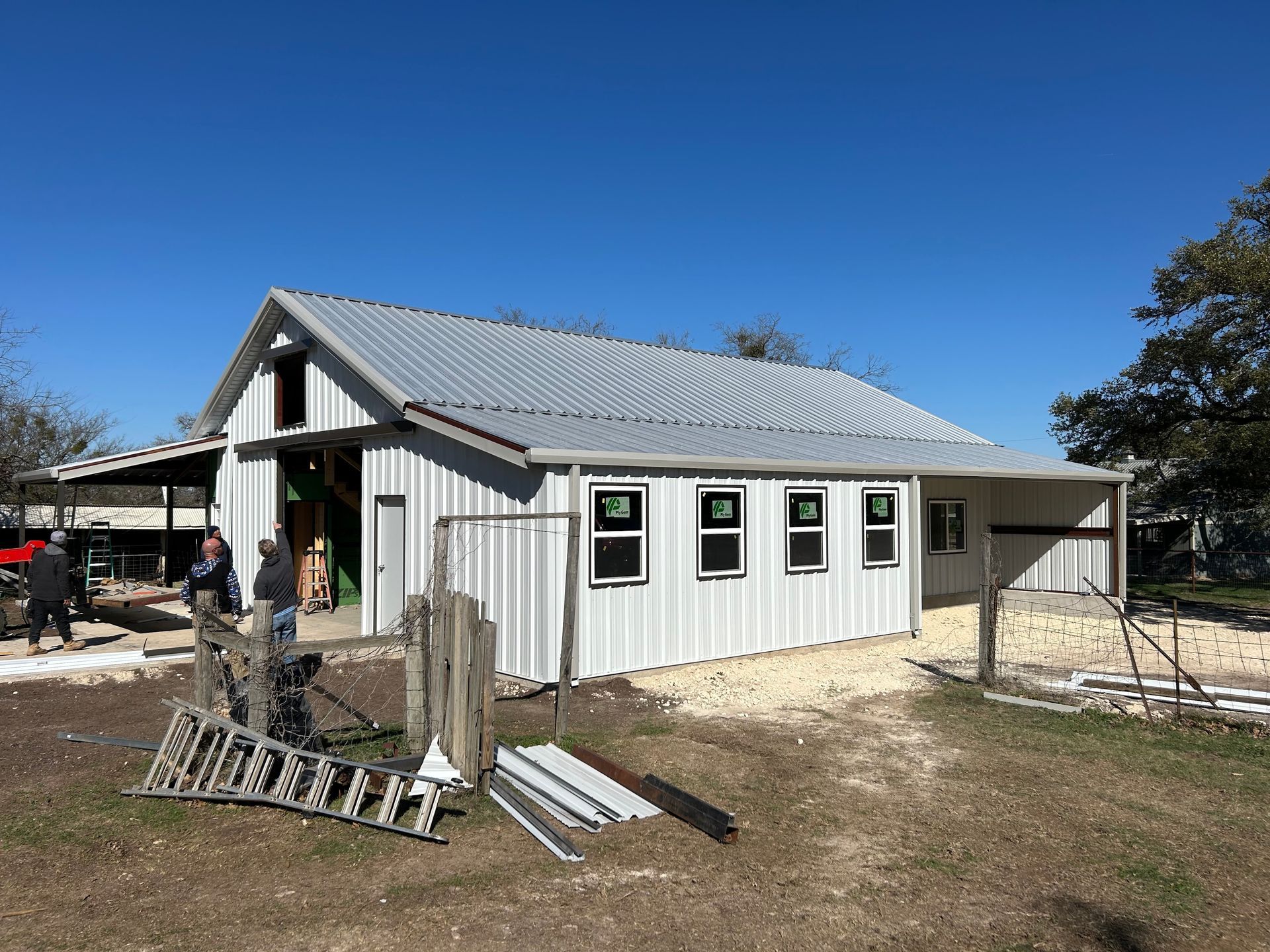 Gray house under construction with white trim and metal roof on a sunny day