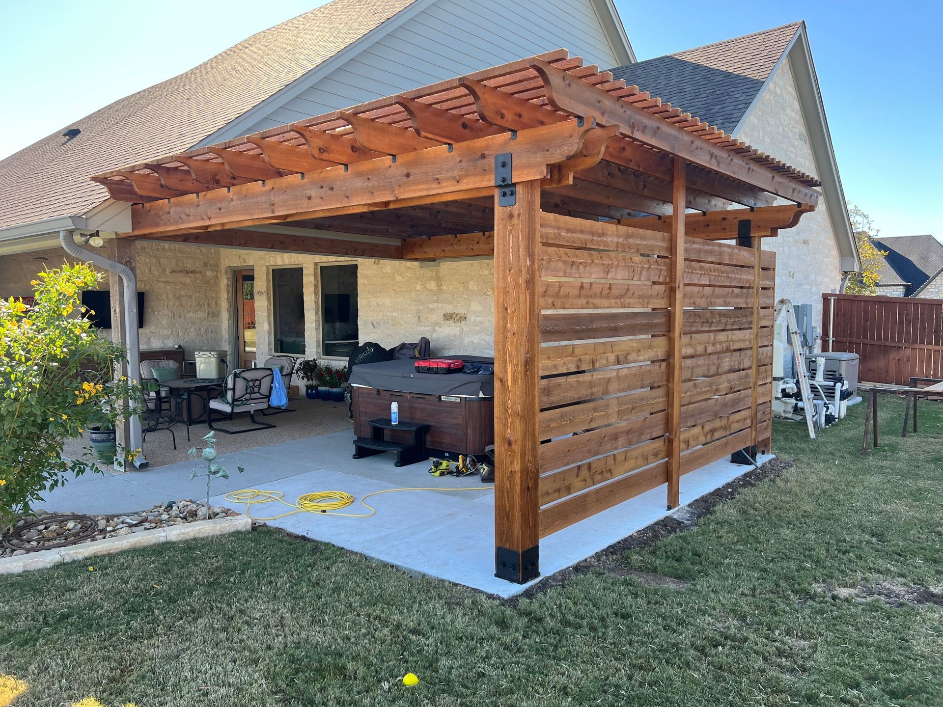Wooden backyard pergola with slatted privacy wall and covered seating area on a concrete patio