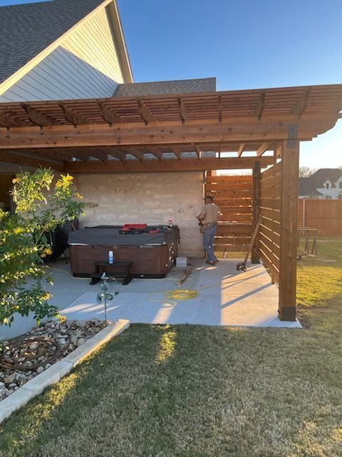 Backyard patio with a covered wooden pergola, hot tub, and a person standing by the wall