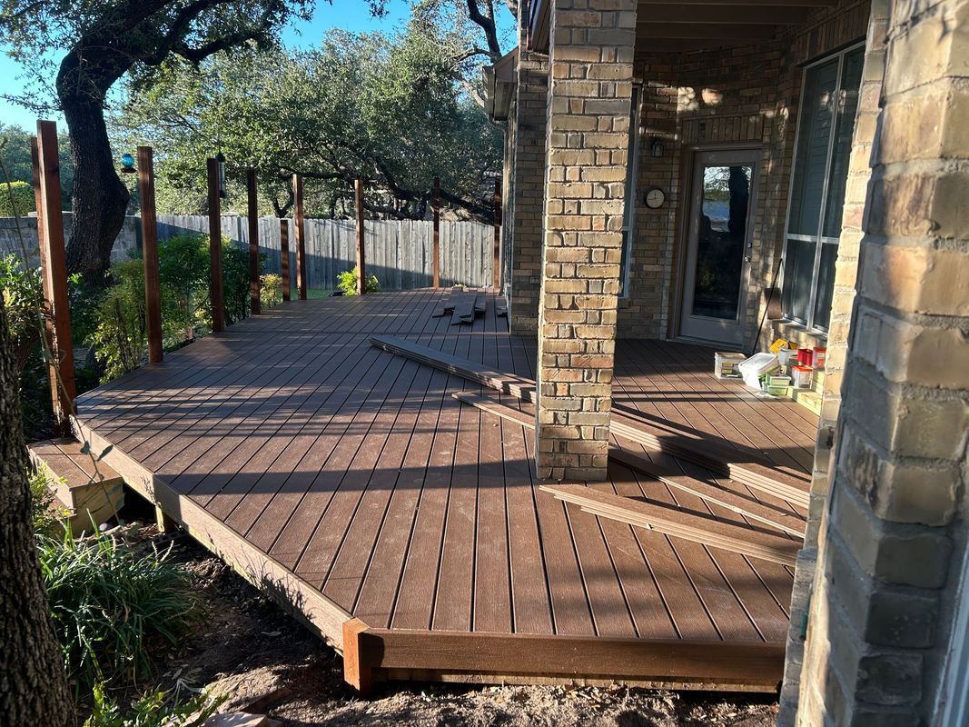 Curved wooden deck porch with stone columns and a view of trees and a walkway outdoors